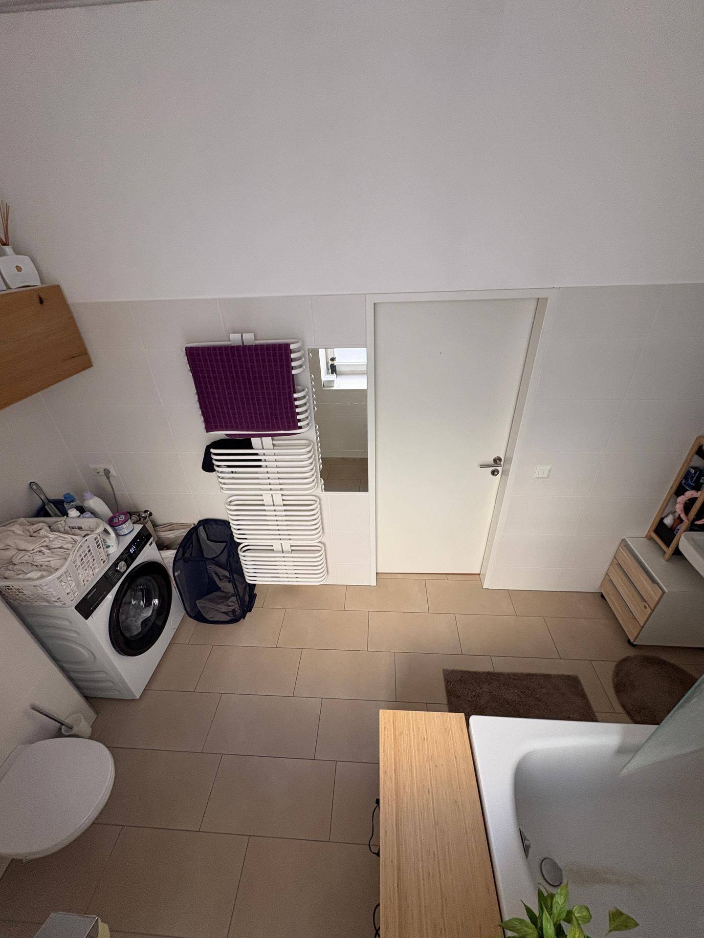 Geräumiges Badezimmer mit Toilette, Waschmaschine, Badewanne und beheiztem Handtuchhalter.