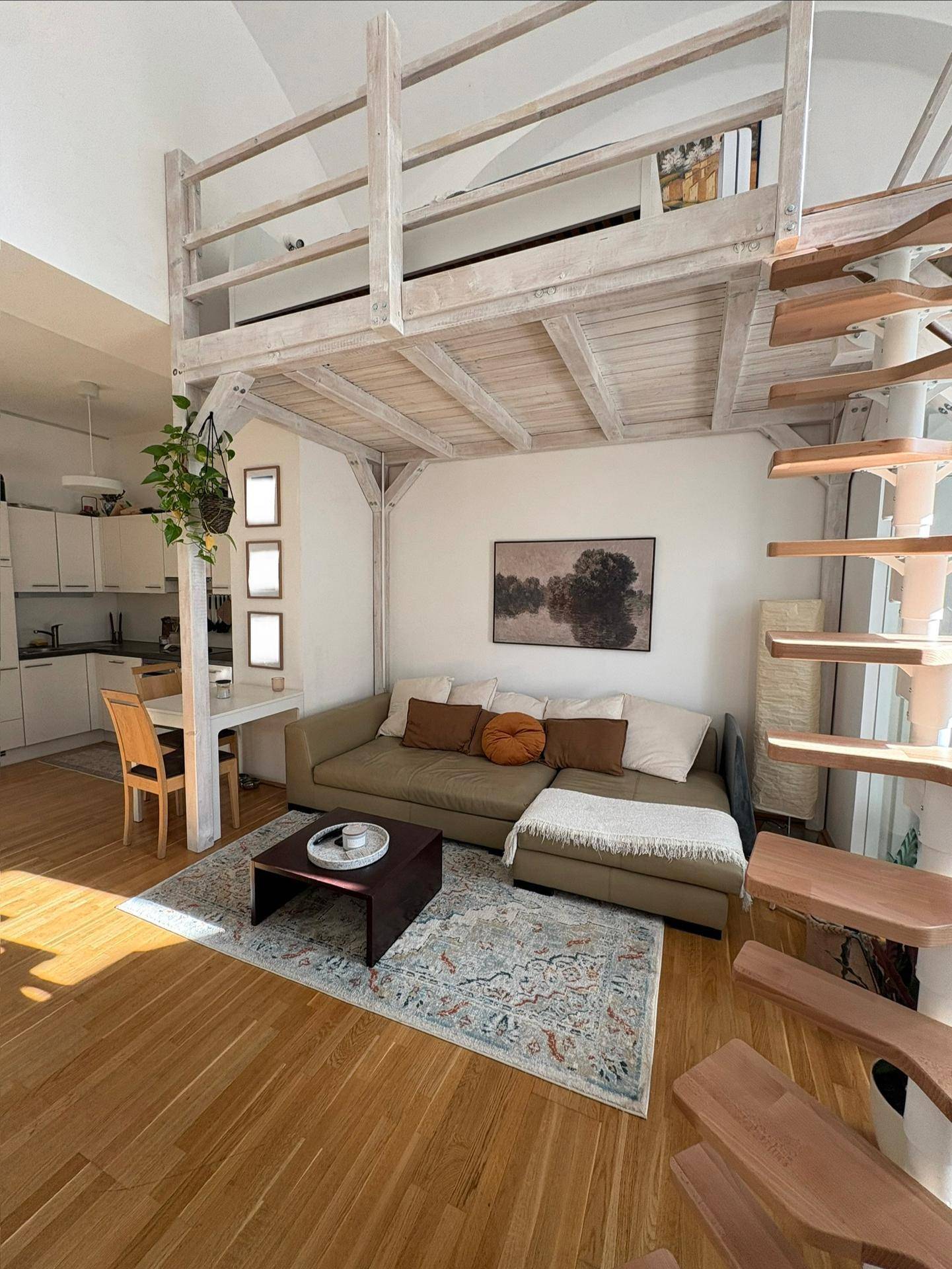 Gemütlicher Wohnbereich mit Sofa, Couchtisch und einem Holz-Loftbett darüber, offen zur Küche.