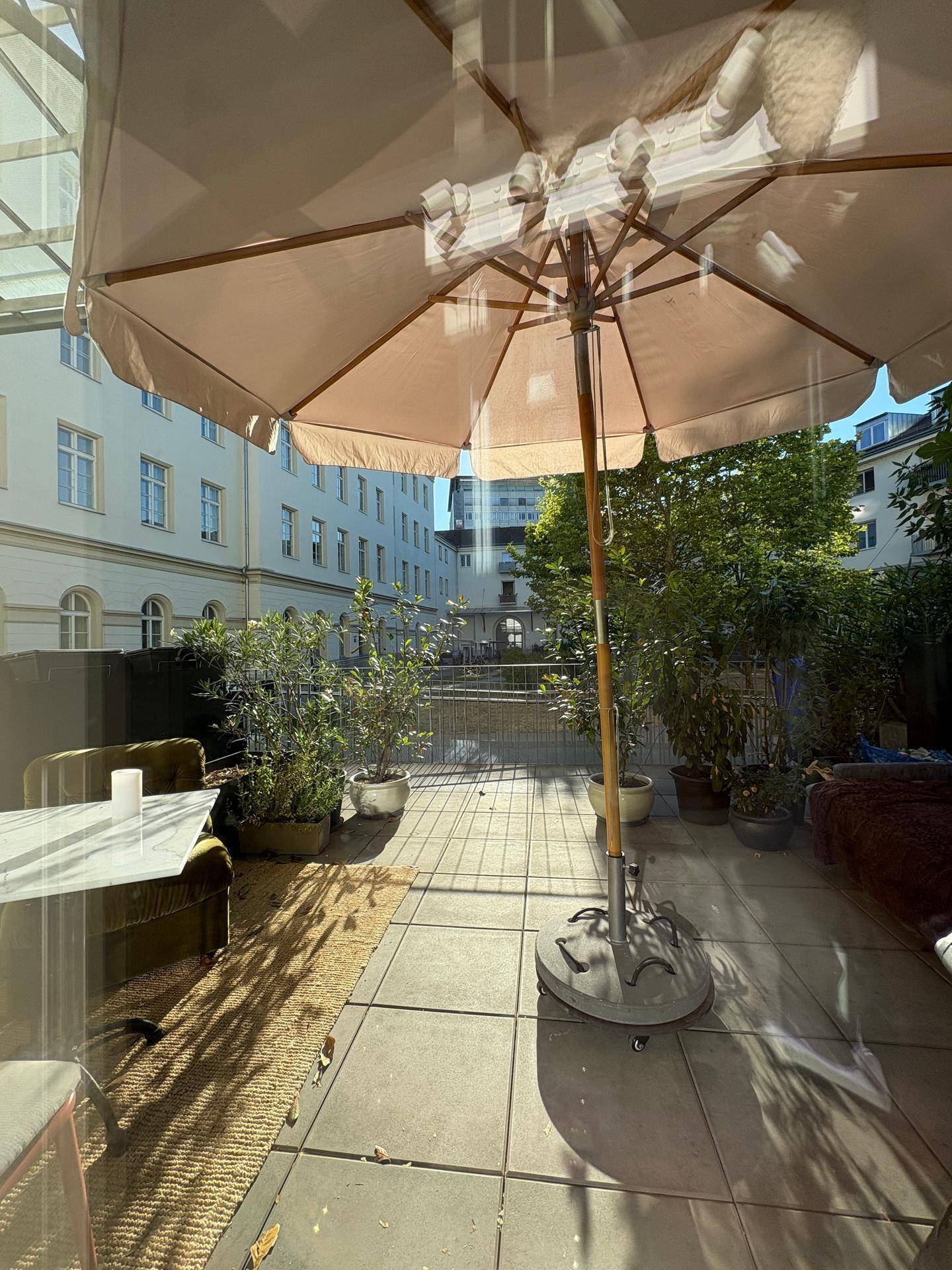 Große Terrasse mit Sitzgelegenheiten, Pflanzen und Blick auf die umliegenden Gebäude.