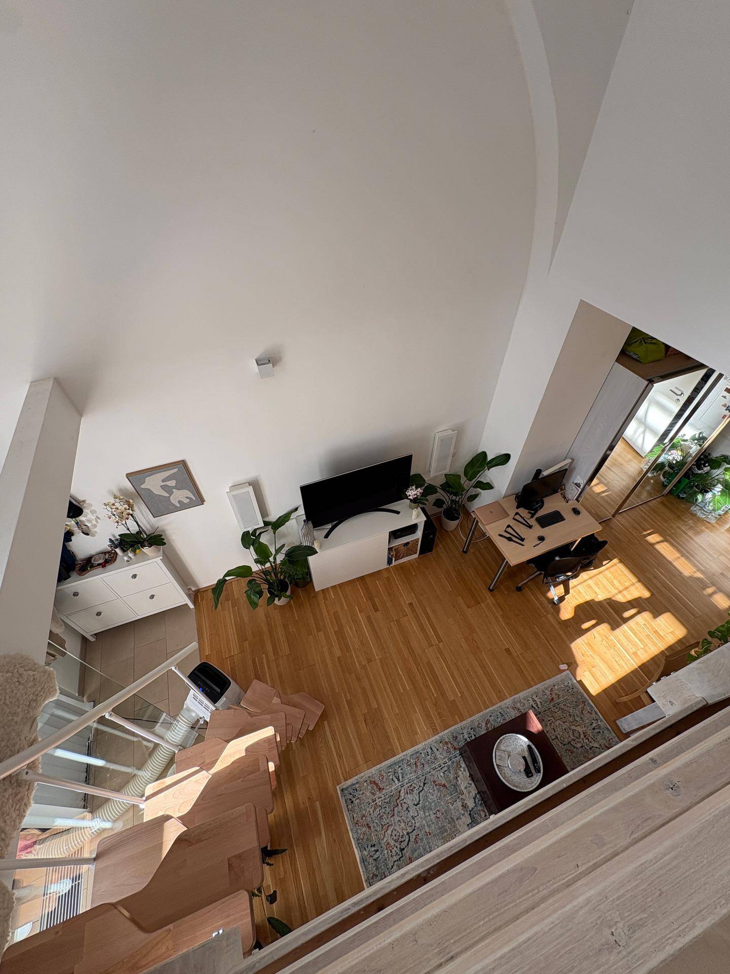 Blick von oben auf den offenen Wohnbereich mit Arbeitsplatz, Fernseher und Sofa.