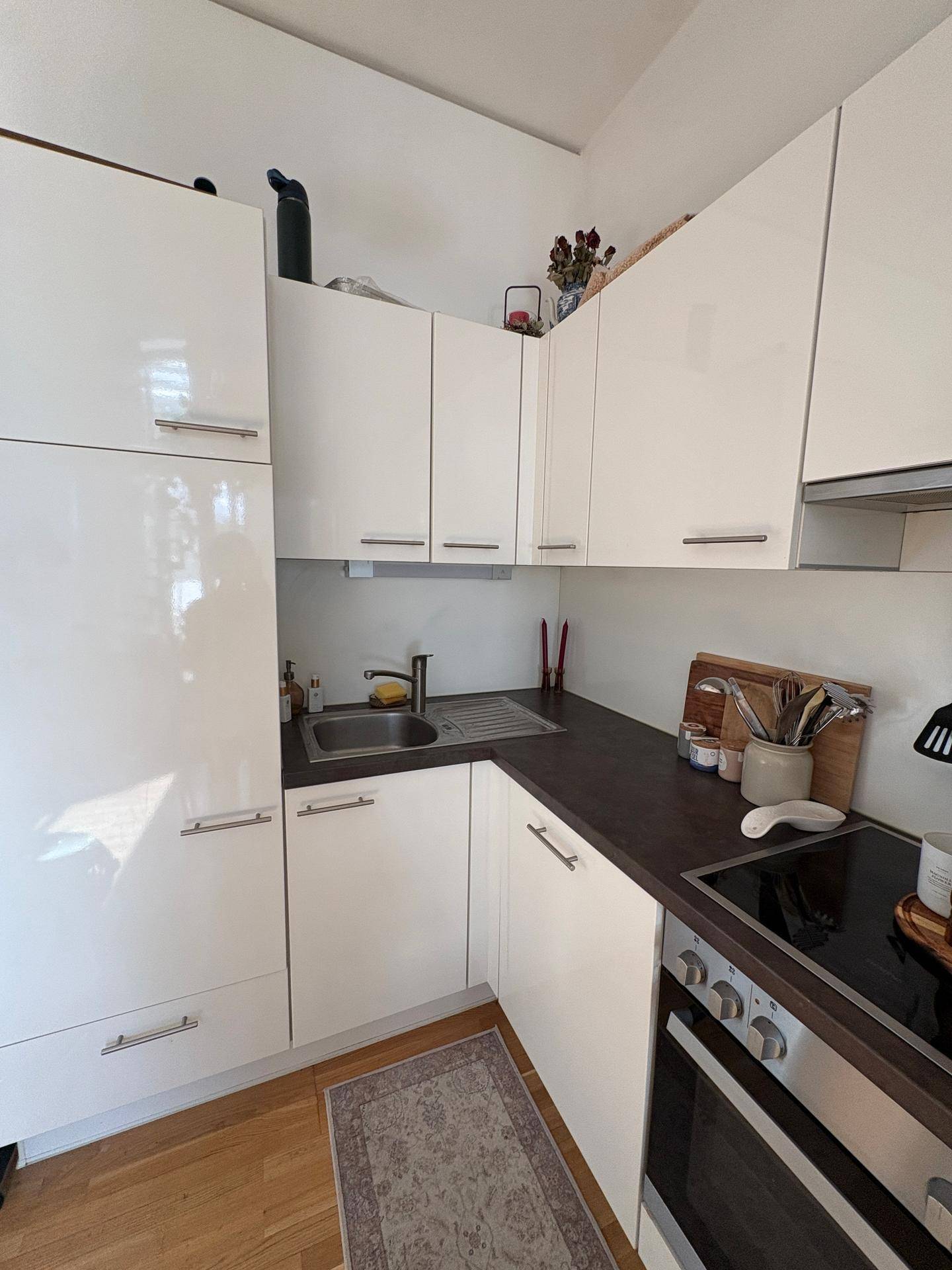 Detailansicht der modernen Küche mit Spüle, Kochfeld, Backofen und weißen Hochglanzschränken.
