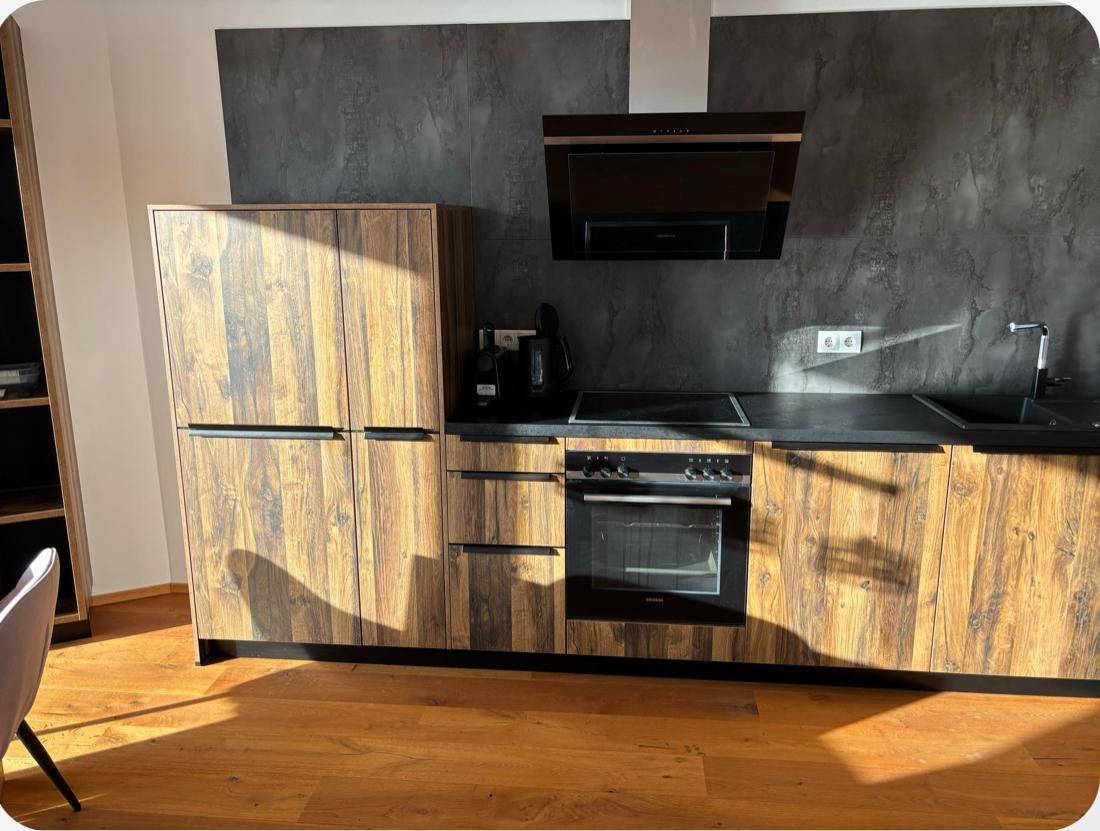 Moderne Küche mit Holzfronten, schwarzer Arbeitsplatte, integrierten Geräten und Dunstabzugshaube.