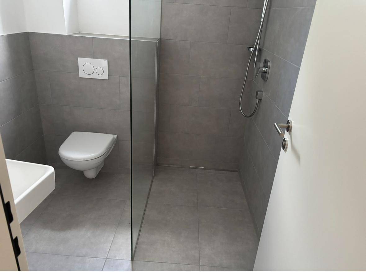 Modernes Badezimmer mit begehbarer Dusche, wandhängendem WC und grauen Fliesen.