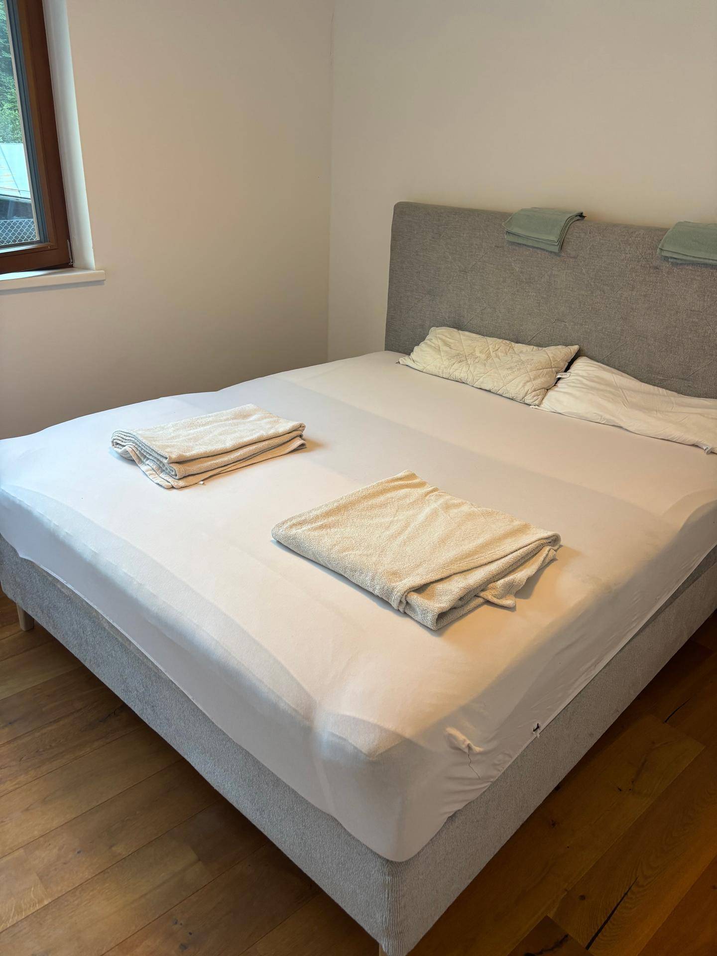 Helles Schlafzimmer mit Doppelbett, weißen Laken und Handtüchern, sowie einem Fenster für natürliches Licht.
