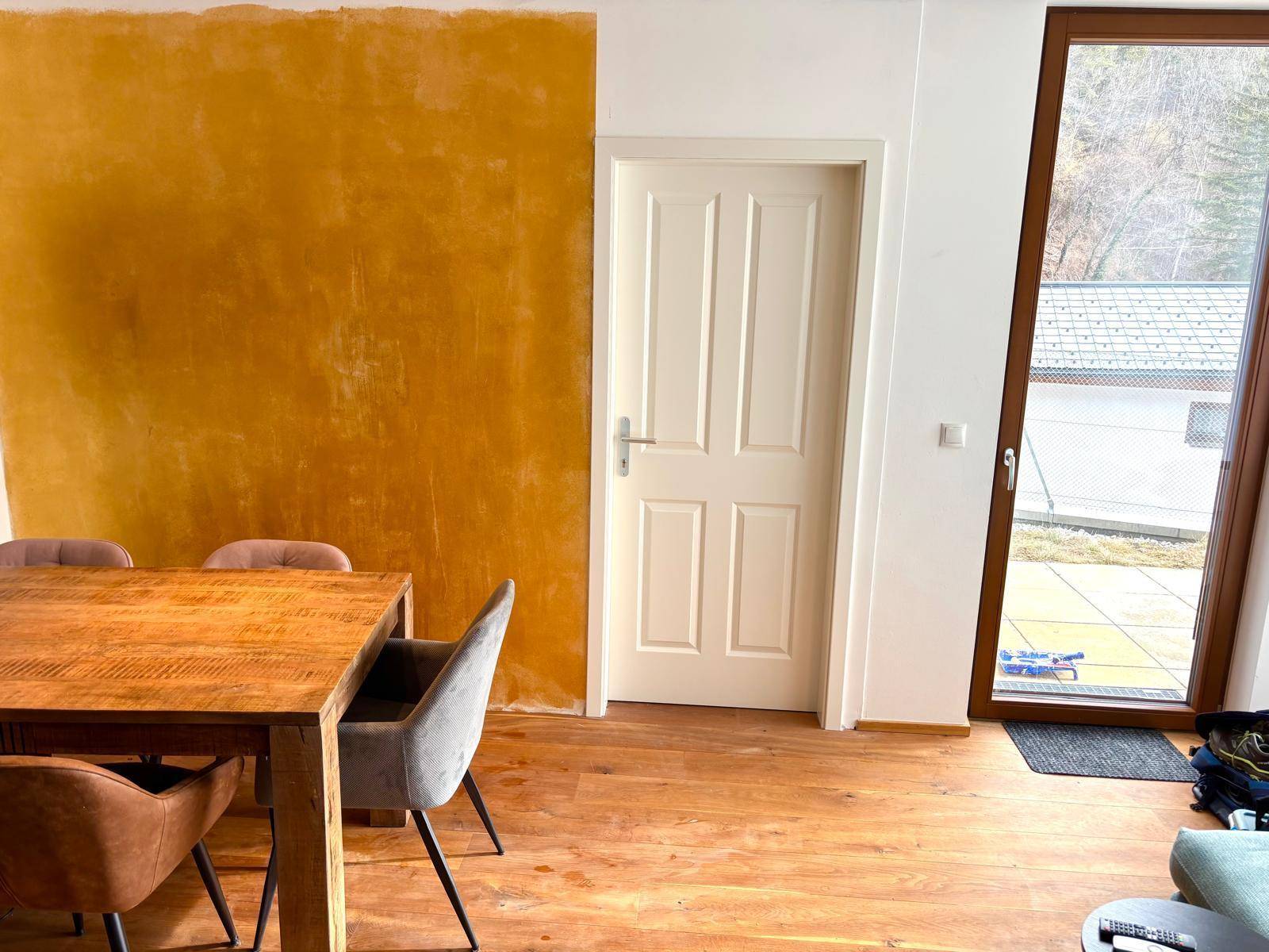 Essbereich mit Holztisch, modernen Stühlen und einer auffälligen gelben Wand neben der Tür und dem Fenster.