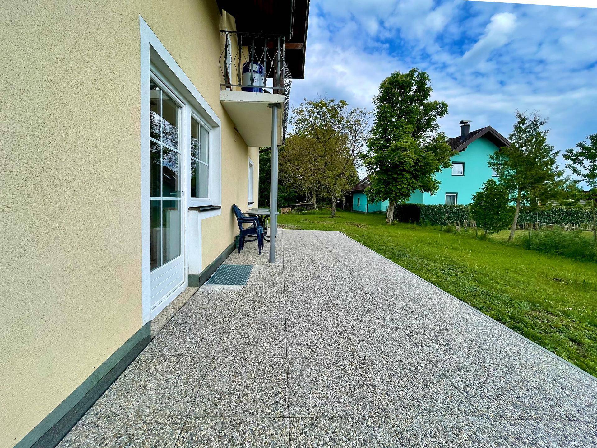 Große gepflasterte Terrasse am Haus mit Blick auf den Garten und ein weiteres Gebäude.