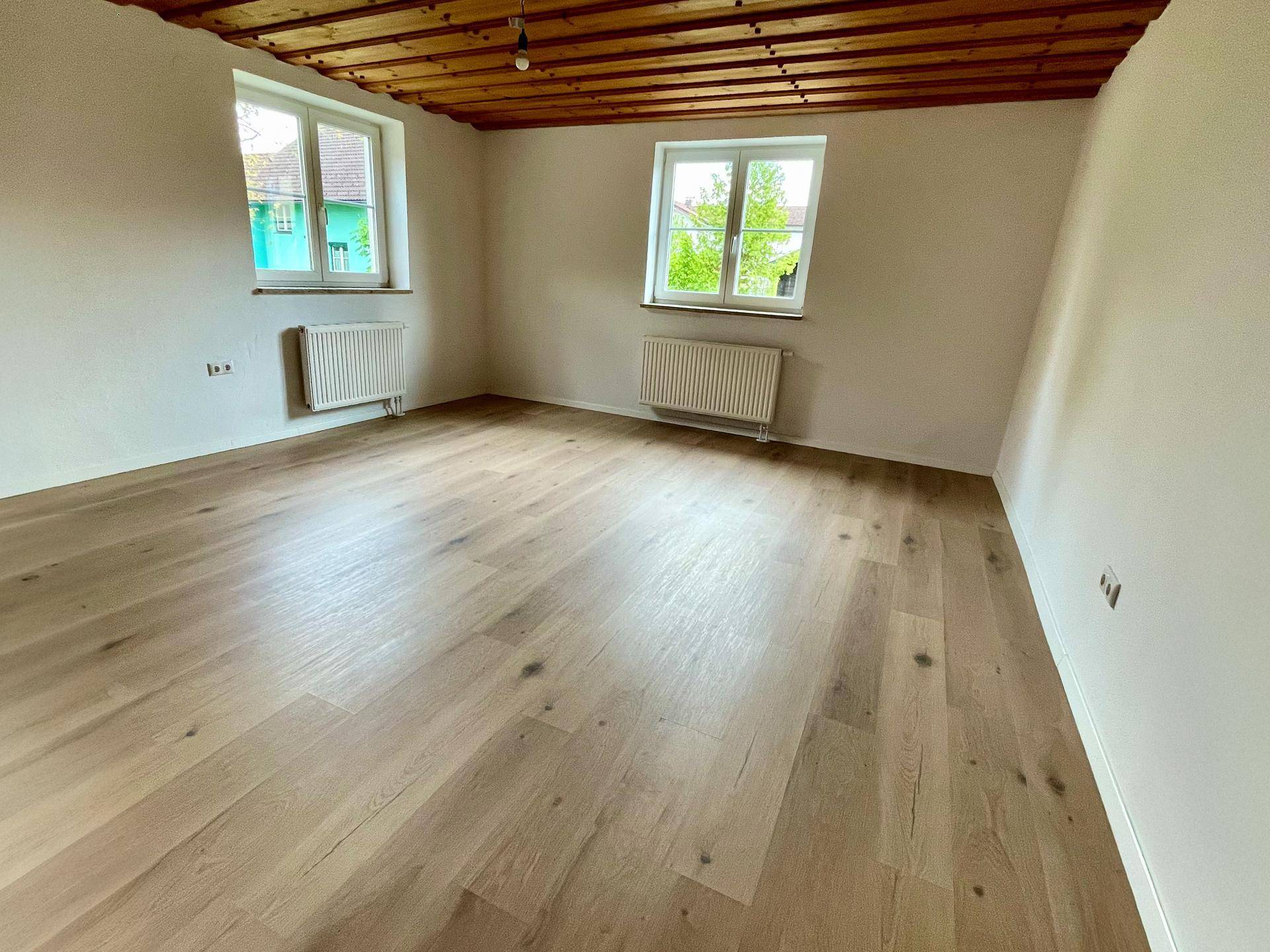 Lichtdurchflutetes Zimmer mit Holzbalkendecke und glänzendem Holzboden, ideal als Schlaf- oder Wohnbereich.