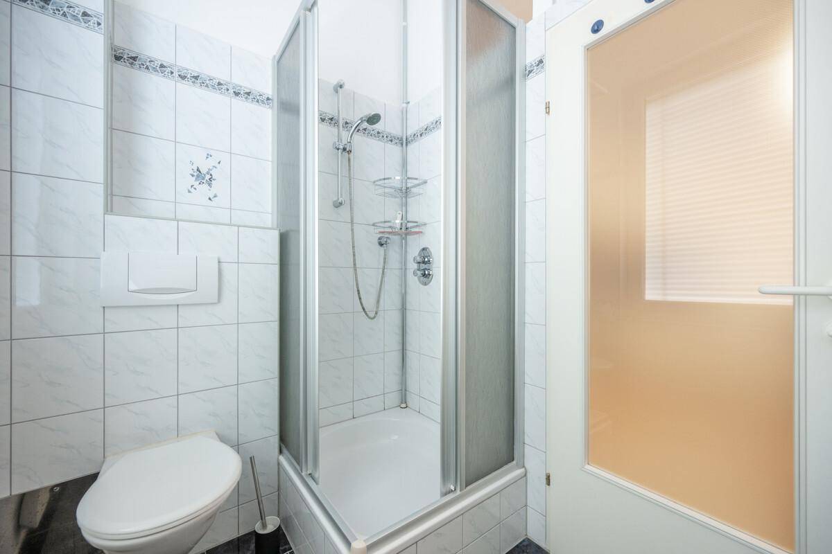 Badezimmer mit Duschkabine, WC und weißen Fliesen, akzentuiert durch eine blaue Bordüre.