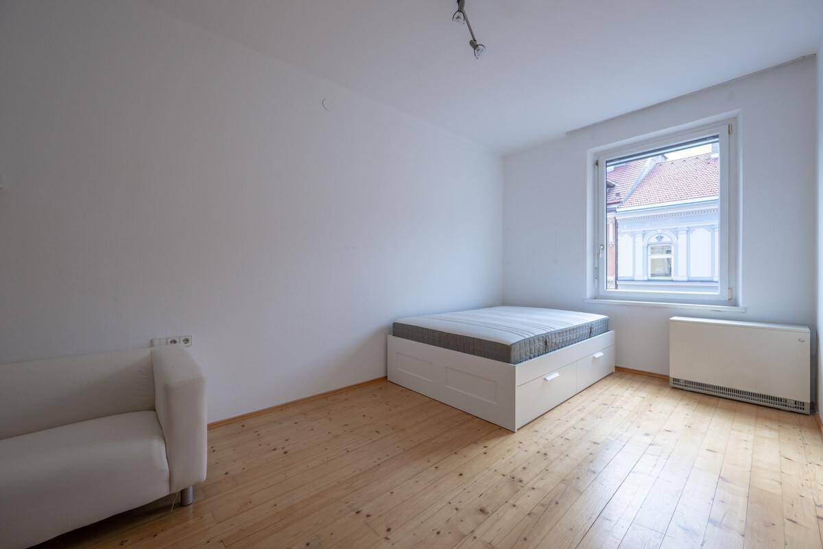Helles Schlafzimmer mit Holzboden, einem Bett mit Stauraum und einem Fenster mit Blick nach draußen.