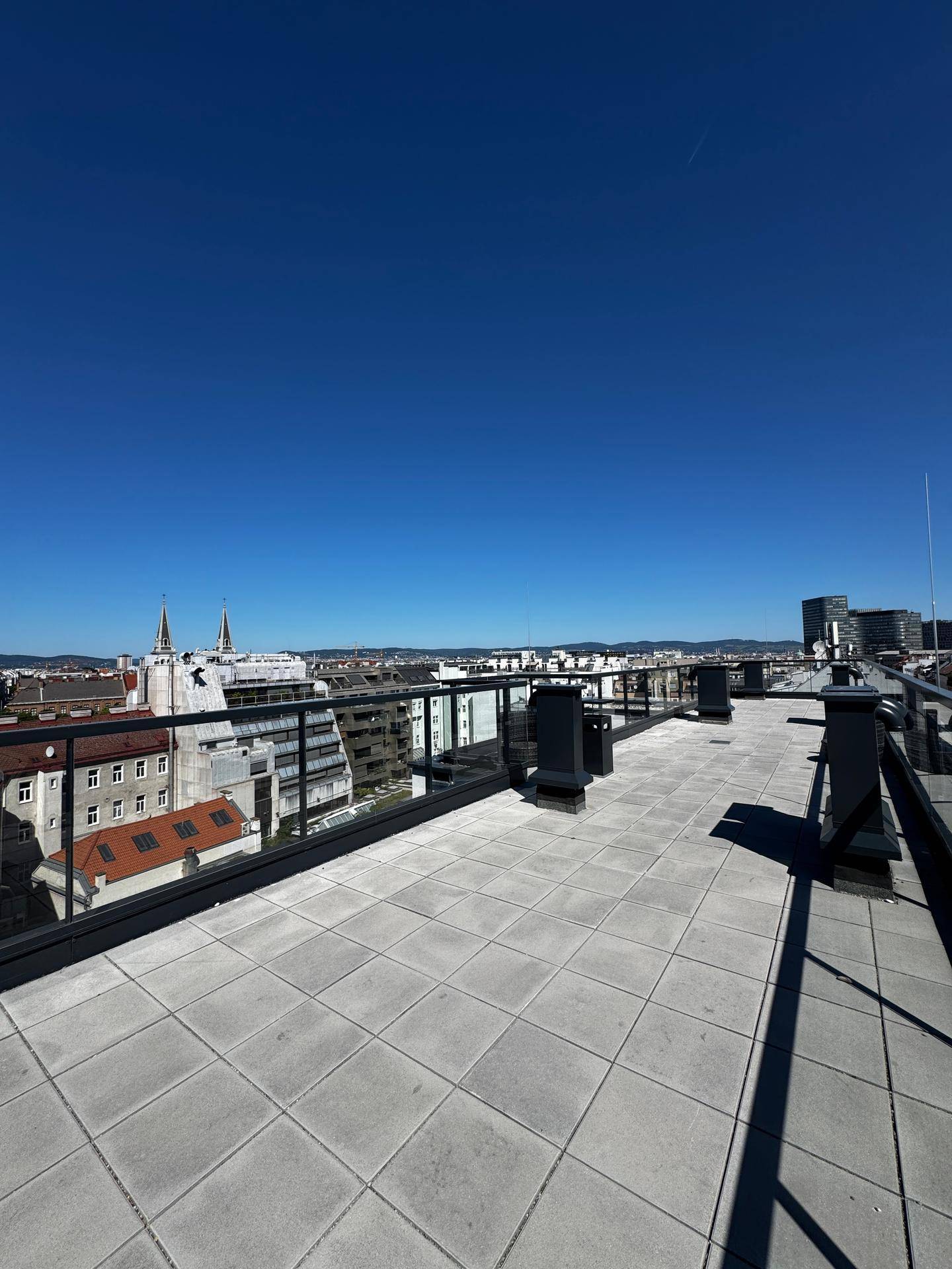 Weitläufige Dachterrasse mit Panoramablick über die Stadt und den blauen Himmel.
