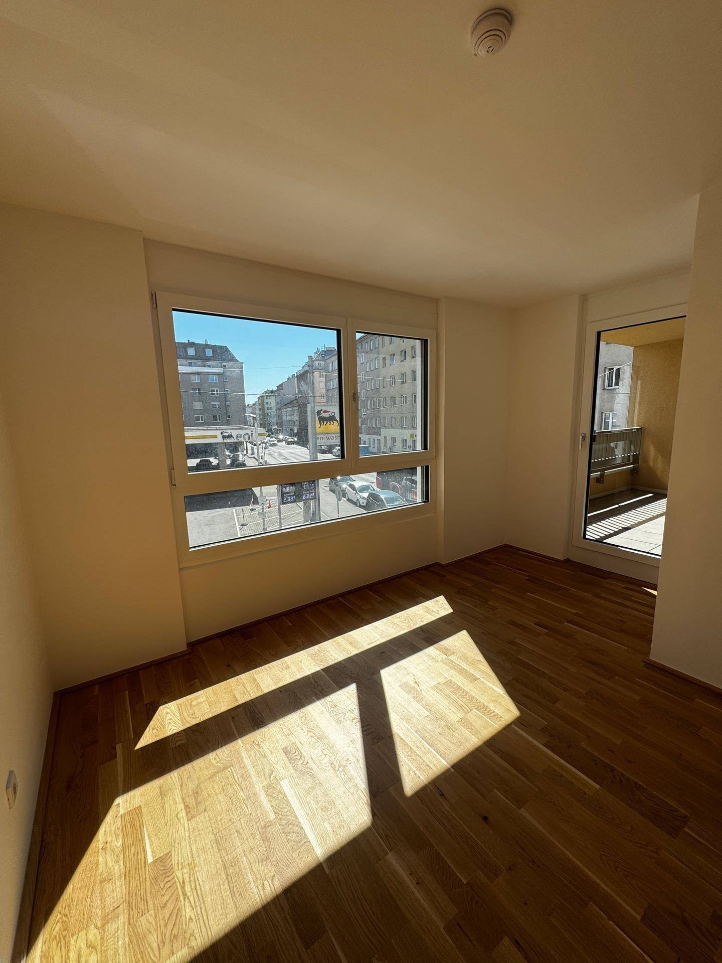 Heller Wohnraum mit Holzboden, großen Fenstern und Zugang zu einem Balkon.