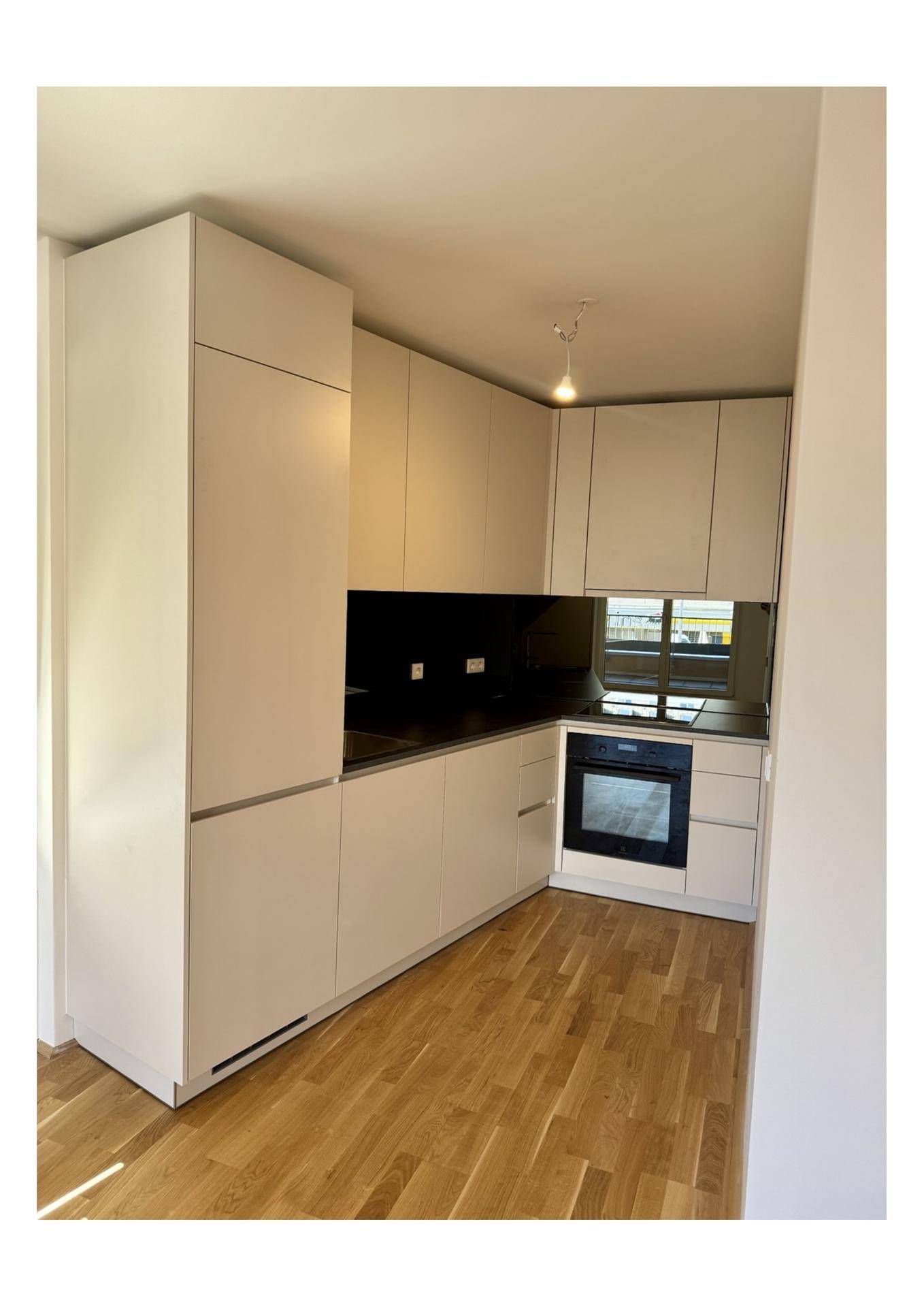 Moderne Einbauküche in hellem Beige mit integriertem Backofen und Holzfußboden.