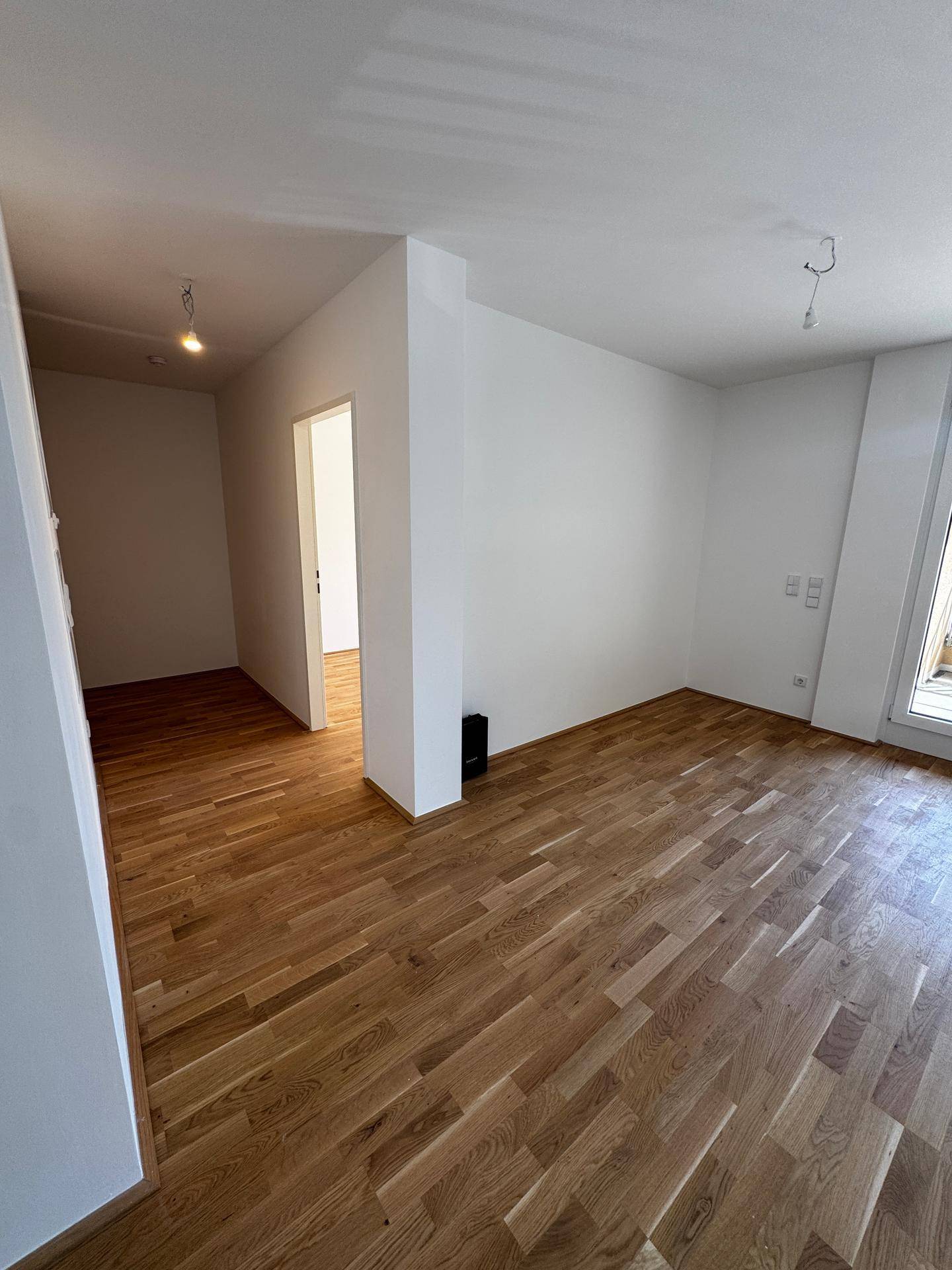 Geräumiger Wohnbereich mit hellem Holzboden und weiß gestrichenen Wänden.