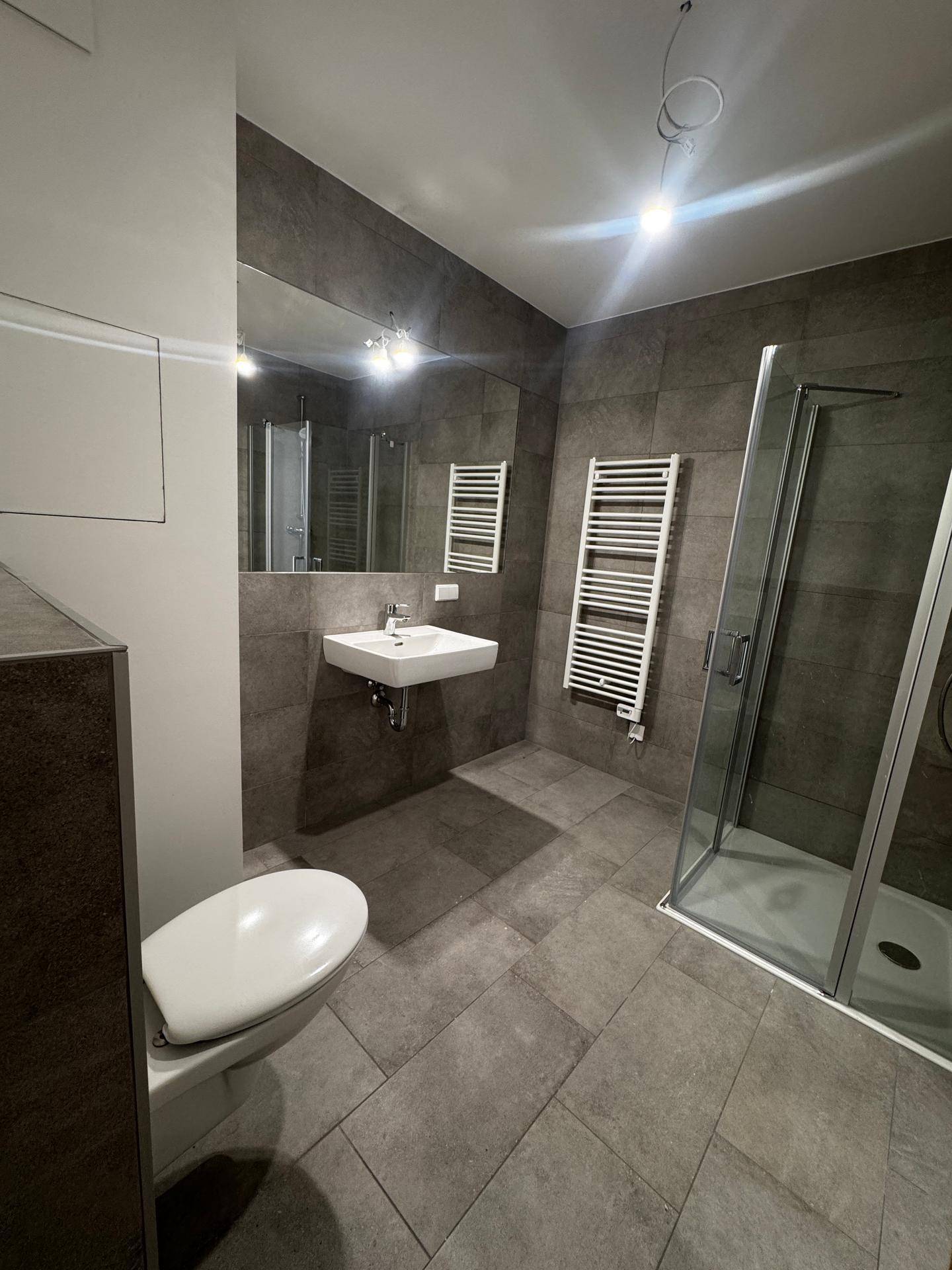 Modernes Badezimmer mit grauen Fliesen, Dusche und beheiztem Handtuchhalter.
