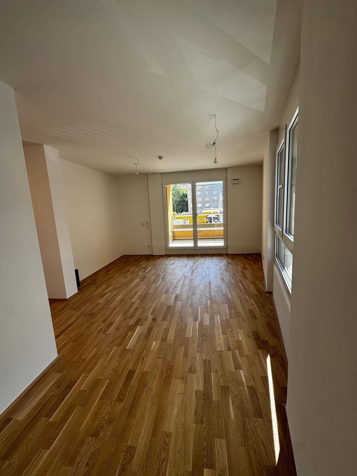 Lichtdurchfluteter Wohnraum mit Holzboden und Blick auf den grünen Außenbereich.
