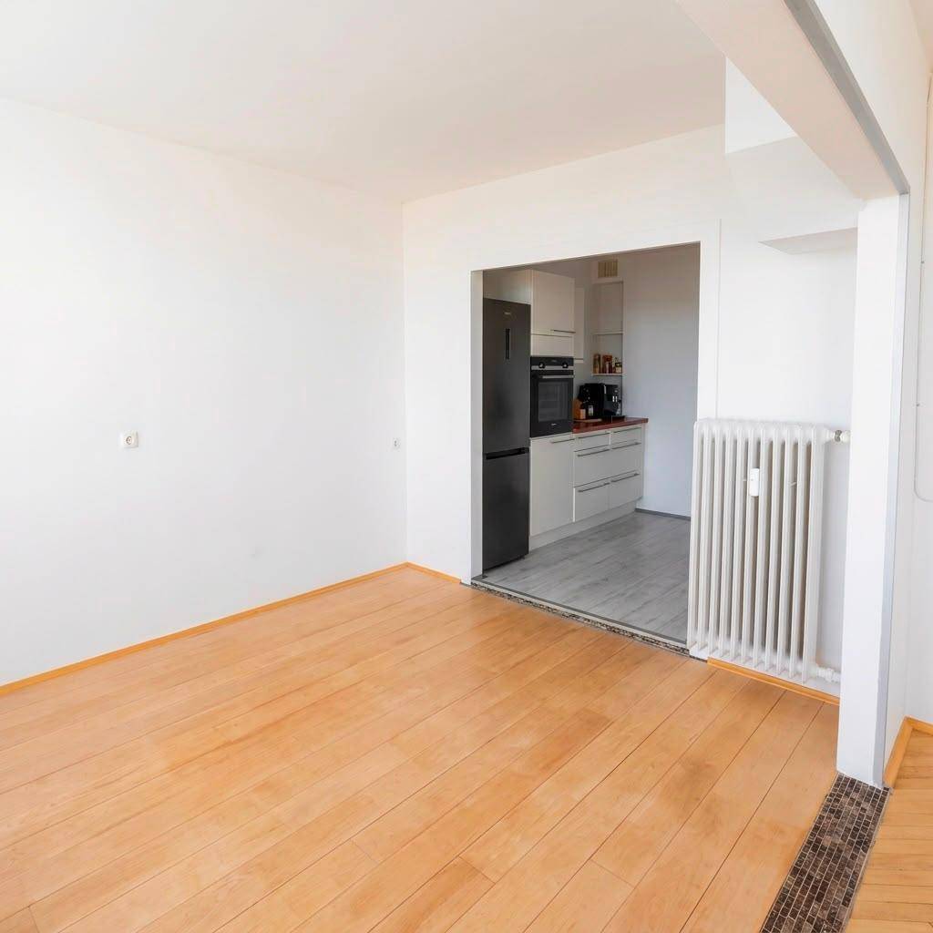 Offener Wohnbereich mit Holzfußboden, Heizkörper und Blick in die angrenzende Küche.