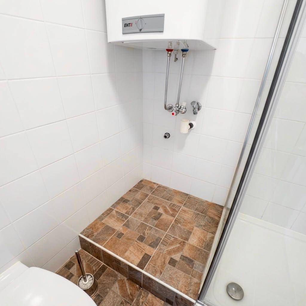 Duschbereich mit gefliestem Boden, Toilette und Warmwasserboiler.