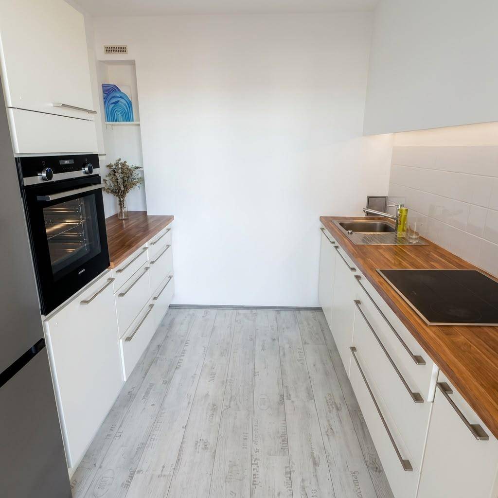 Schmale Küche mit weißen Schränken, Holz-Arbeitsplatten, Einbauofen und Induktionskochfeld.