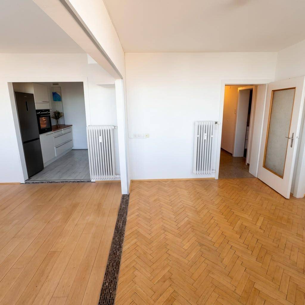 Offener Wohnbereich mit gemischtem Parkettboden, Heizkörpern und Blick in Küche und Nebenraum.