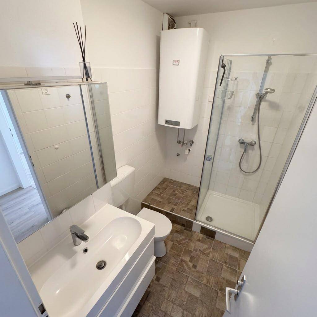 Badezimmer mit Waschbecken, Spiegelschrank, Toilette, Dusche und Warmwasserboiler.