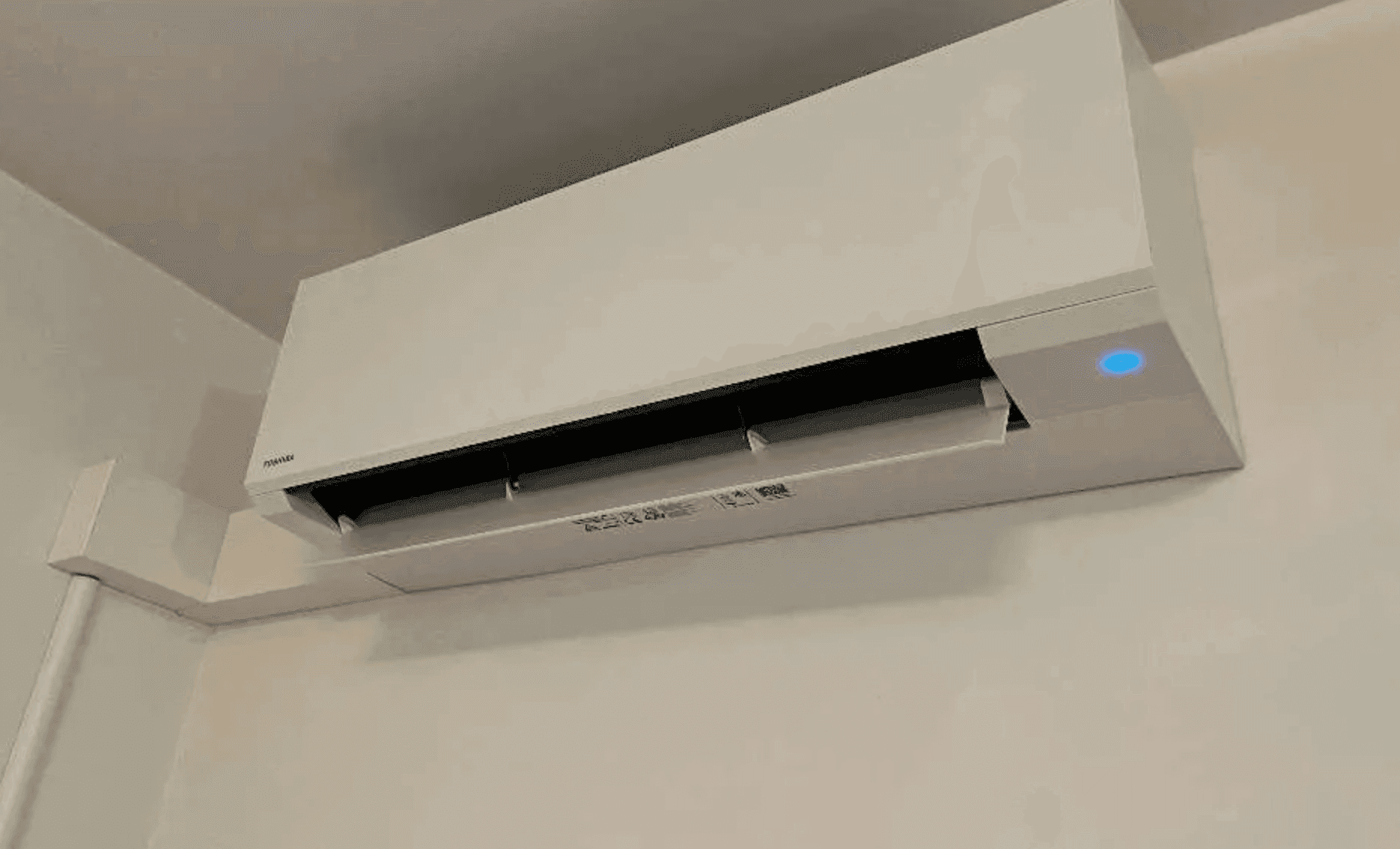 Eine moderne, an der Wand montierte Klimaanlage mit blauer Betriebsanzeige.