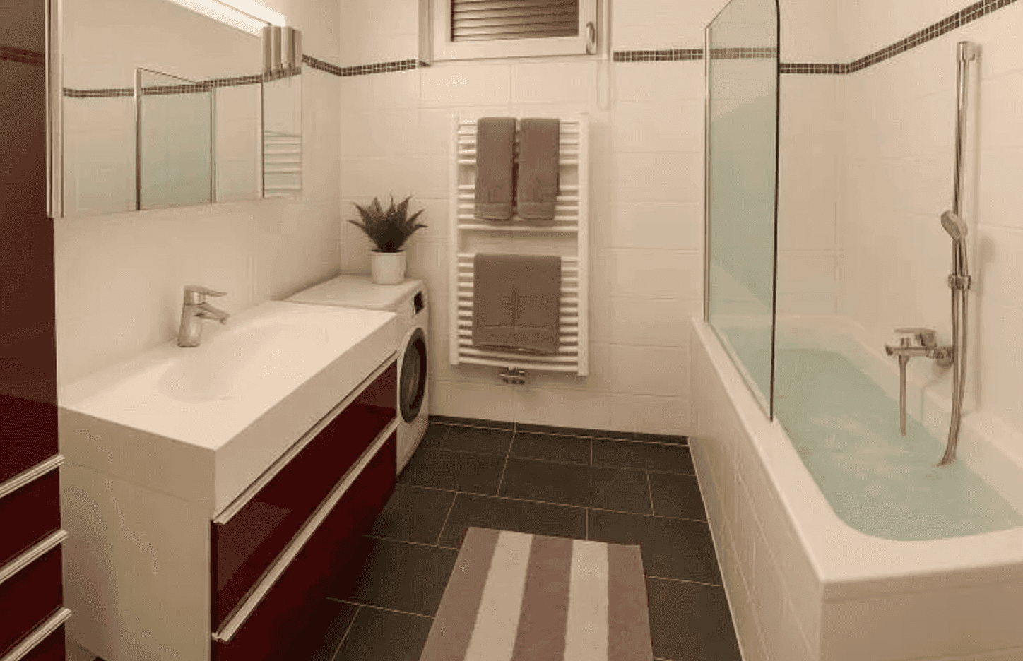 Modernes Badezimmer mit Badewanne, Einzelwaschbecken, beheiztem Handtuchhalter und Waschmaschine.