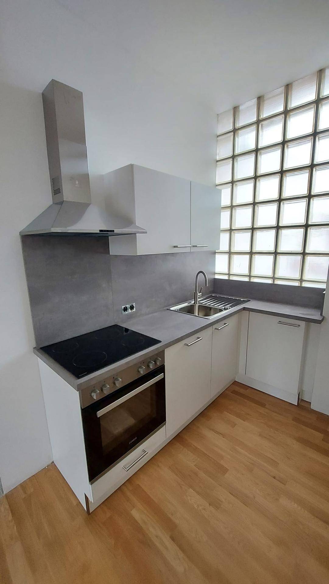 Moderne Einbauküche mit weißen Fronten, Dunstabzugshaube und Glasbausteinfenster.