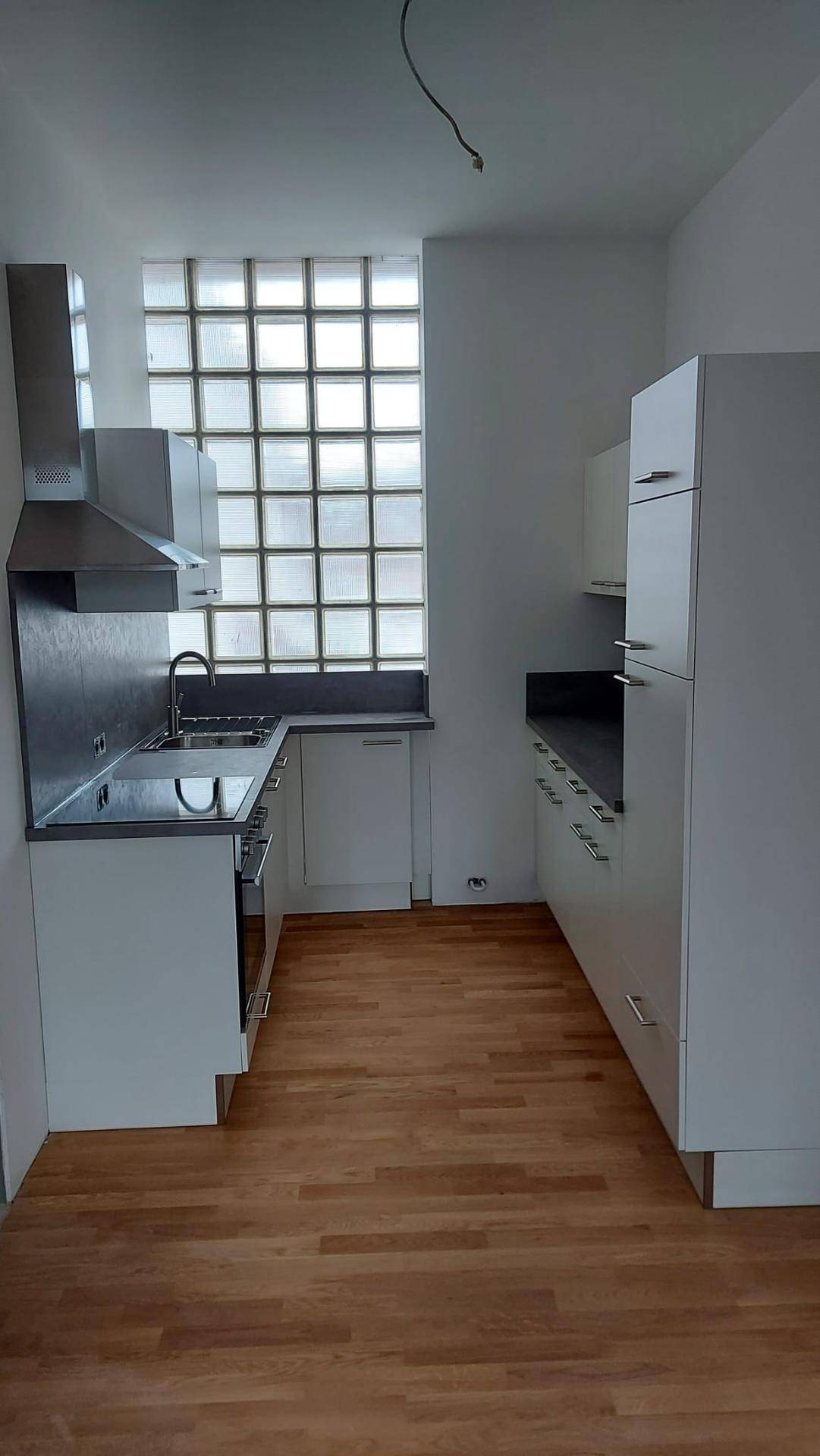Geräumige Küche mit weißen Schränken, Holzparkett und einem großen Glasbausteinfenster.