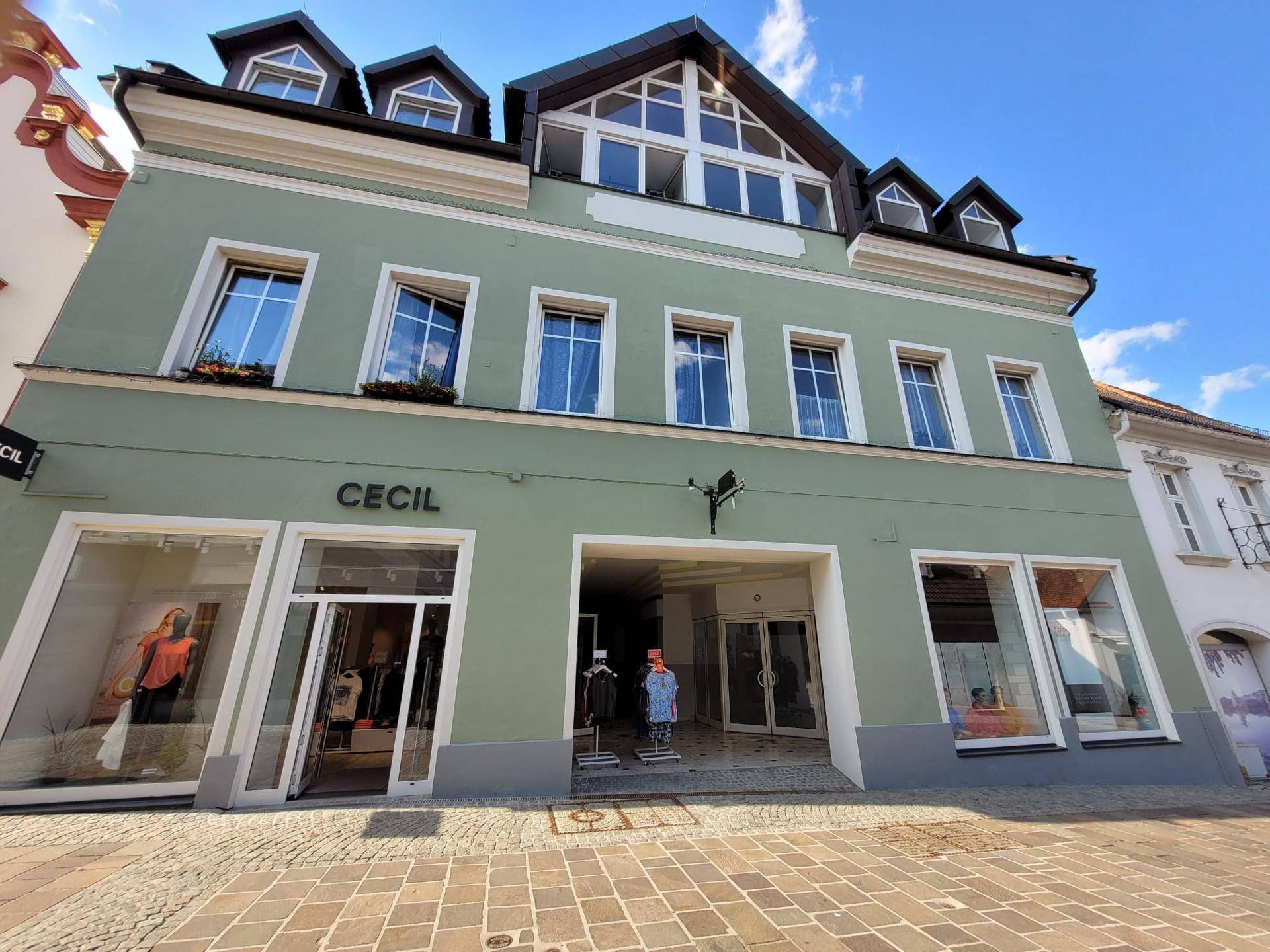 Grüne Fassade eines Geschäftsgebäudes mit großen Schaufenstern und einem Durchgang.