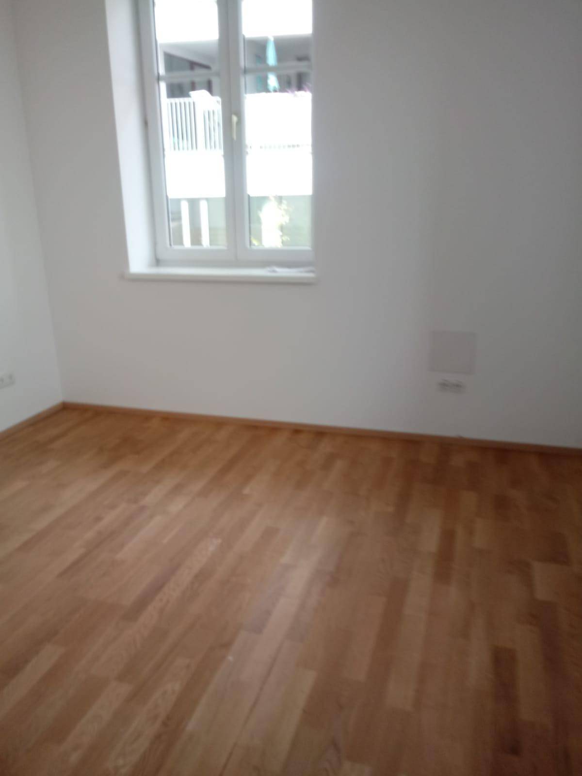 Helles Schlafzimmer mit Holzparkettboden und einem Fenster mit Blick nach draußen.