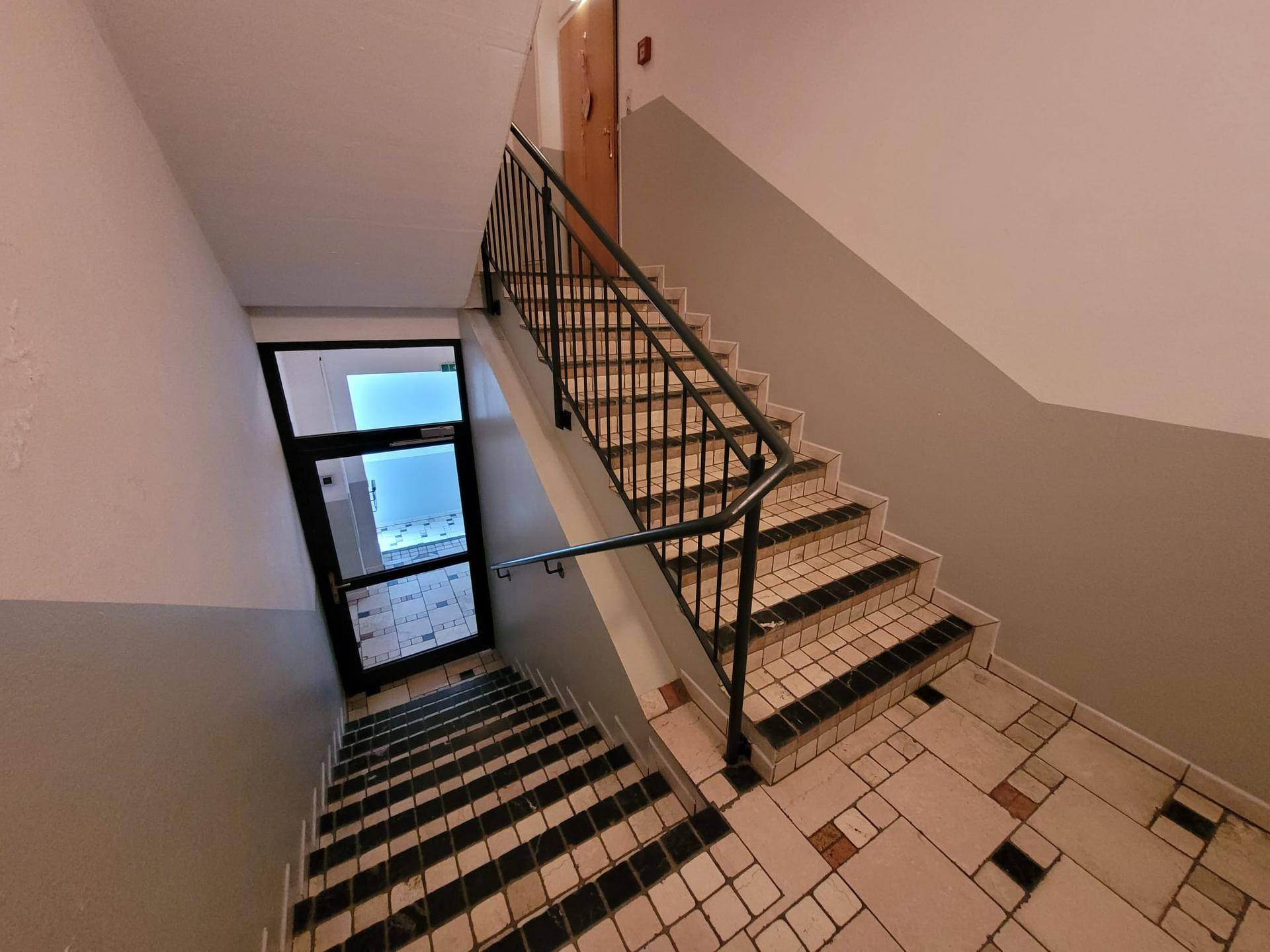 Treppenhaus mit gefliestem Boden und Metallgeländer, das zu den oberen Etagen führt.