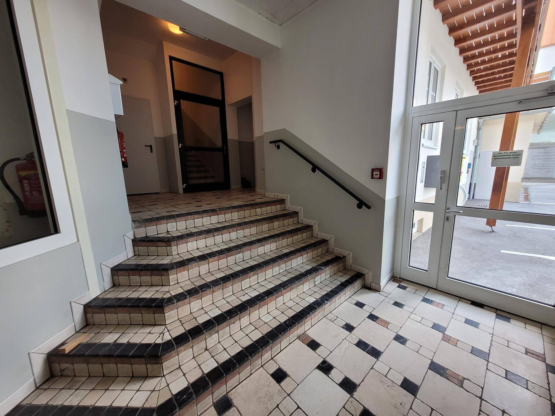 Eingangsbereich mit gefliestem Boden, Treppe und Zugang zum Außenbereich.