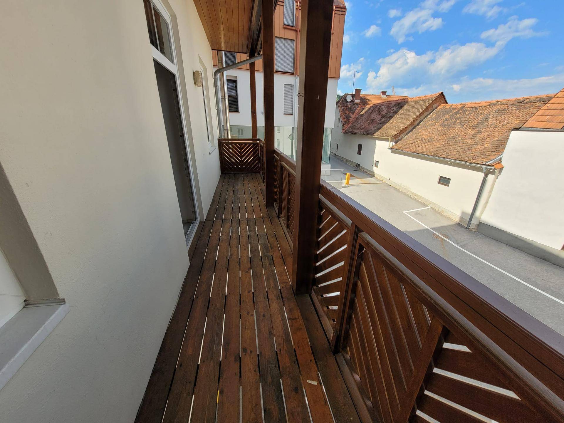Langer Holzbalkon mit Blick auf die umliegenden Gebäude und die Straße.