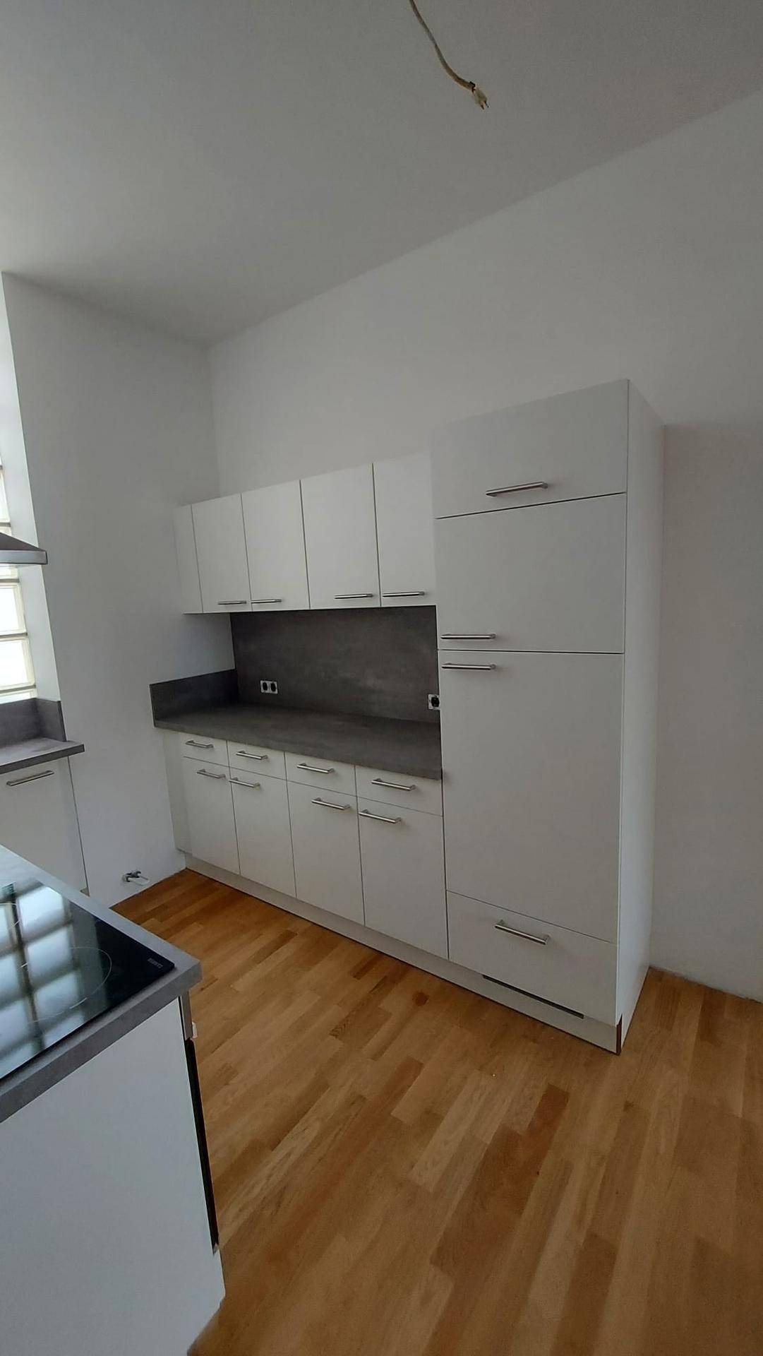 Helle Küche mit weißen Schränken, dunkler Arbeitsplatte und Holzparkettboden.