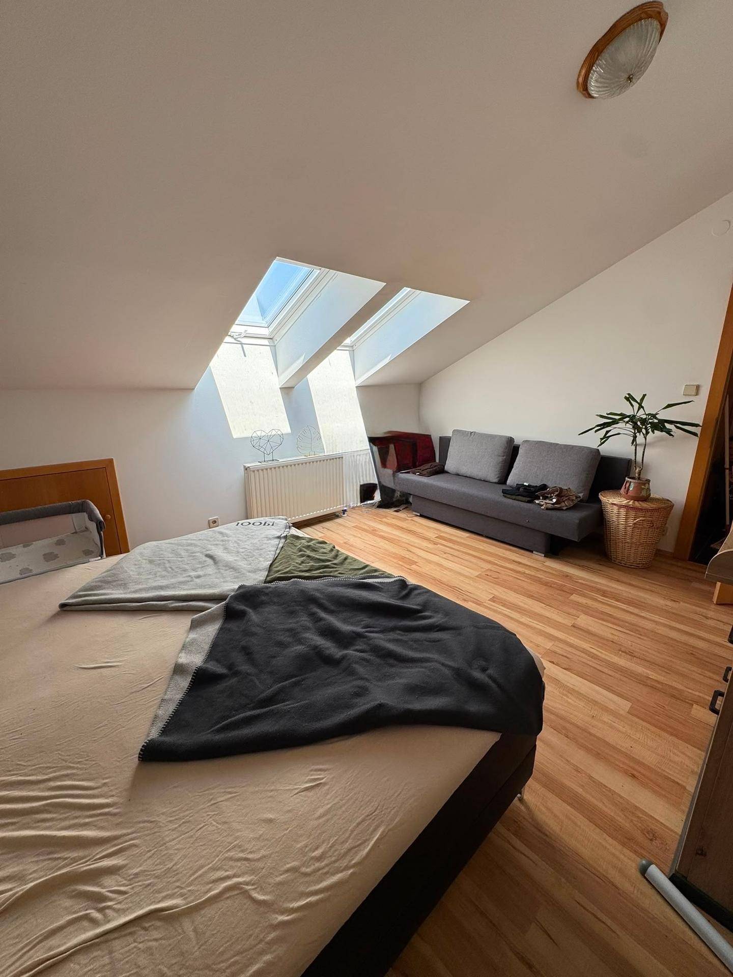 Gemütliches Schlafzimmer im Dachgeschoss mit Bett, Sofa und zwei Dachfenstern für Helligkeit.