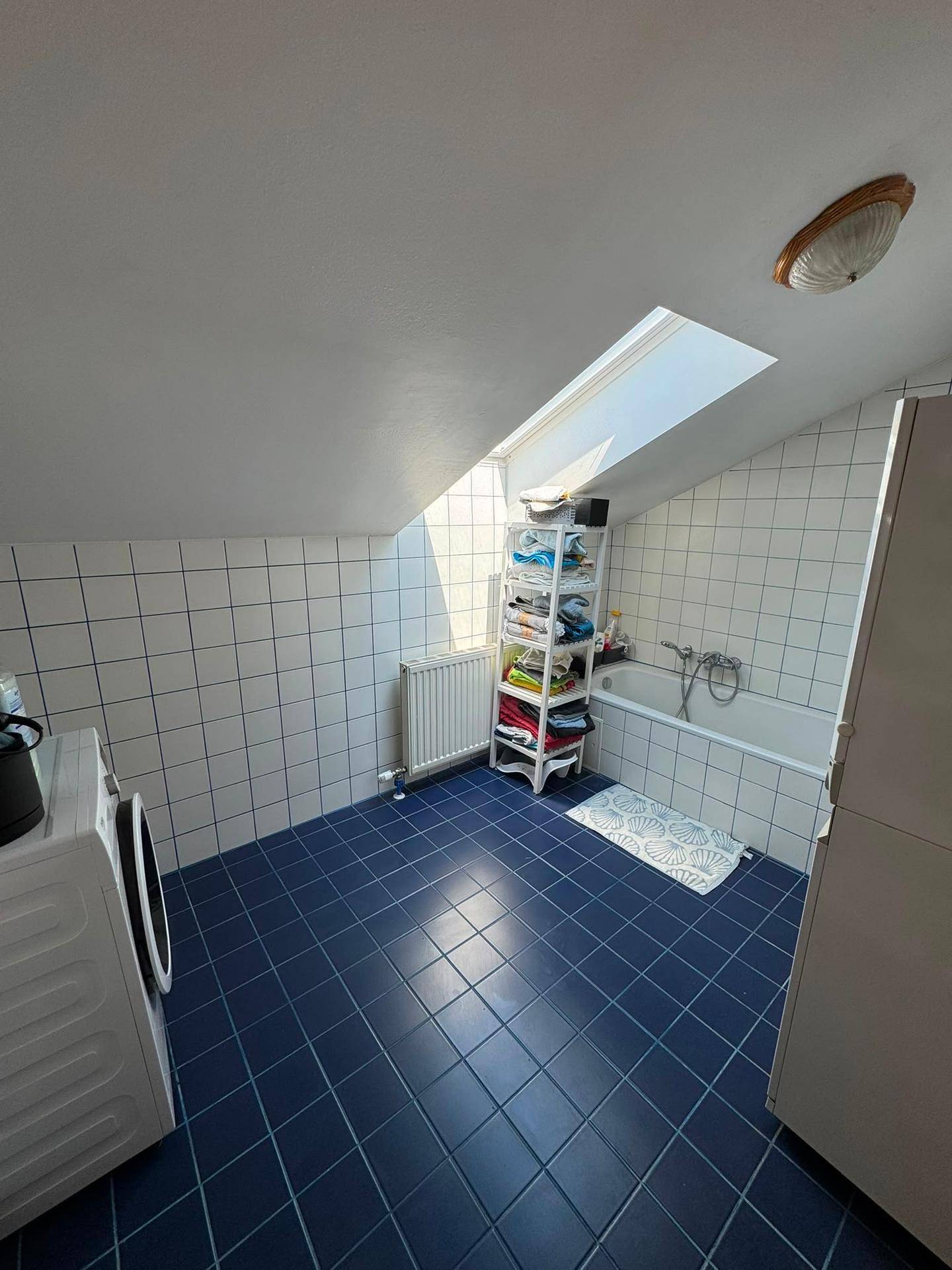 Badezimmer im Dachgeschoss mit Badewanne, Waschmaschine und Dachfenster für natürliches Licht.