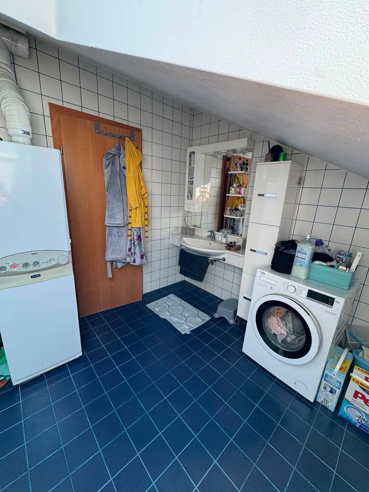 Badezimmer im Dachgeschoss mit Waschbecken, Spiegelschrank und Waschmaschine, funktional eingerichtet.