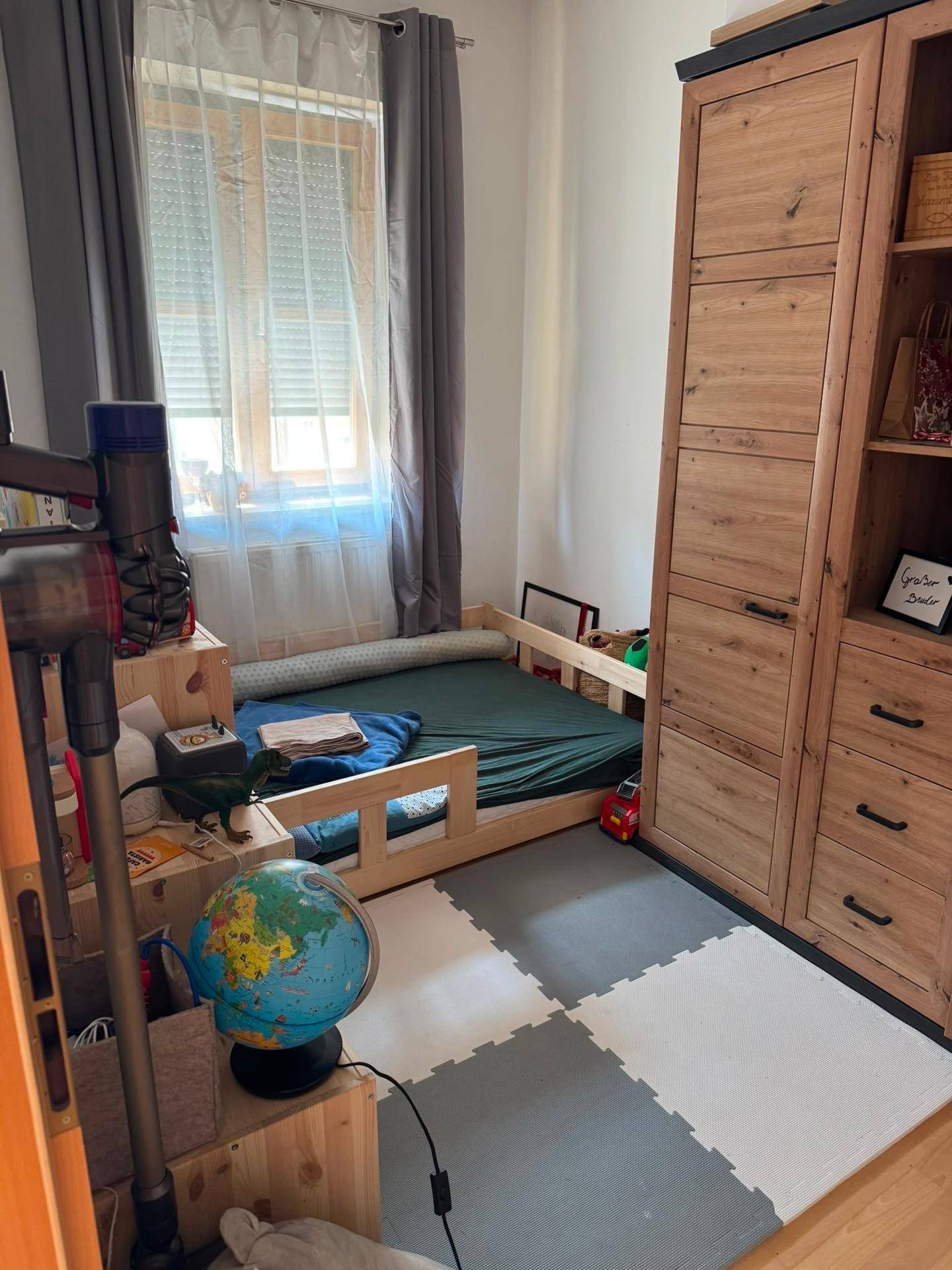 Kinderzimmer mit Bett, Holzschrank und Spielmatte, bietet eine helle und freundliche Atmosphäre.