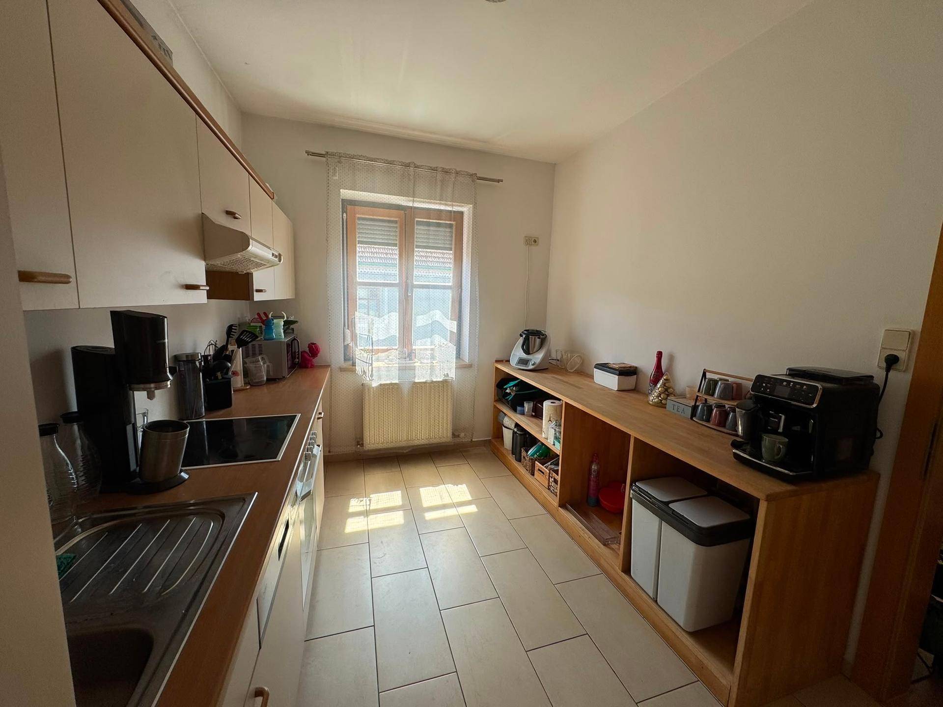 Funktionale Küche mit hellen Schränken, Holz-Arbeitsplatten und einem Fenster mit Jalousien.