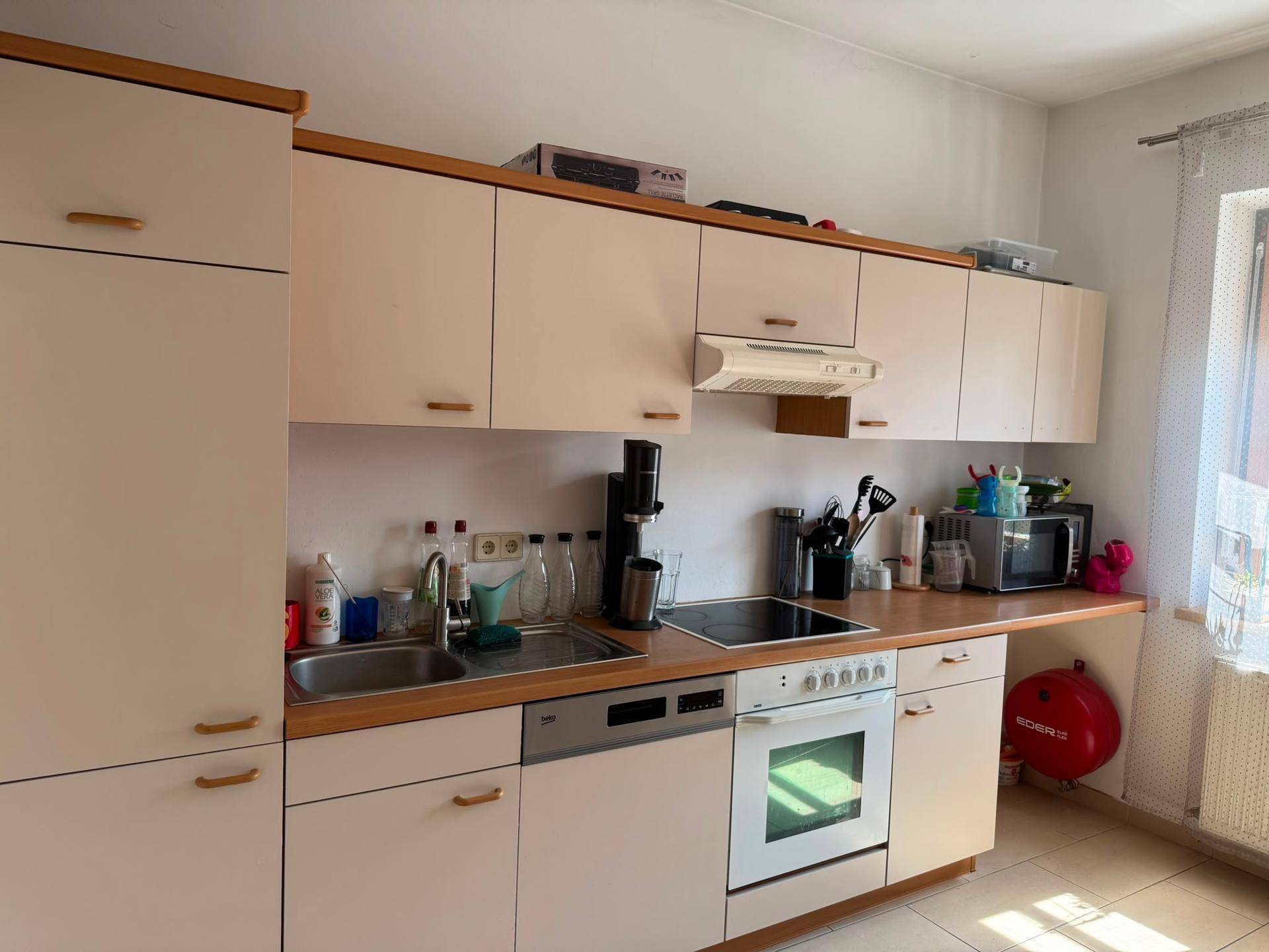 Funktionale Küche mit hellen Schränken, Holz-Arbeitsplatten, Spülmaschine und Backofen.