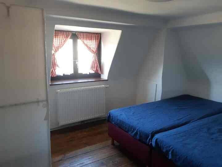 Schlafzimmer mit zwei Einzelbetten, Holzfußboden und Fenster mit karierten Vorhängen.