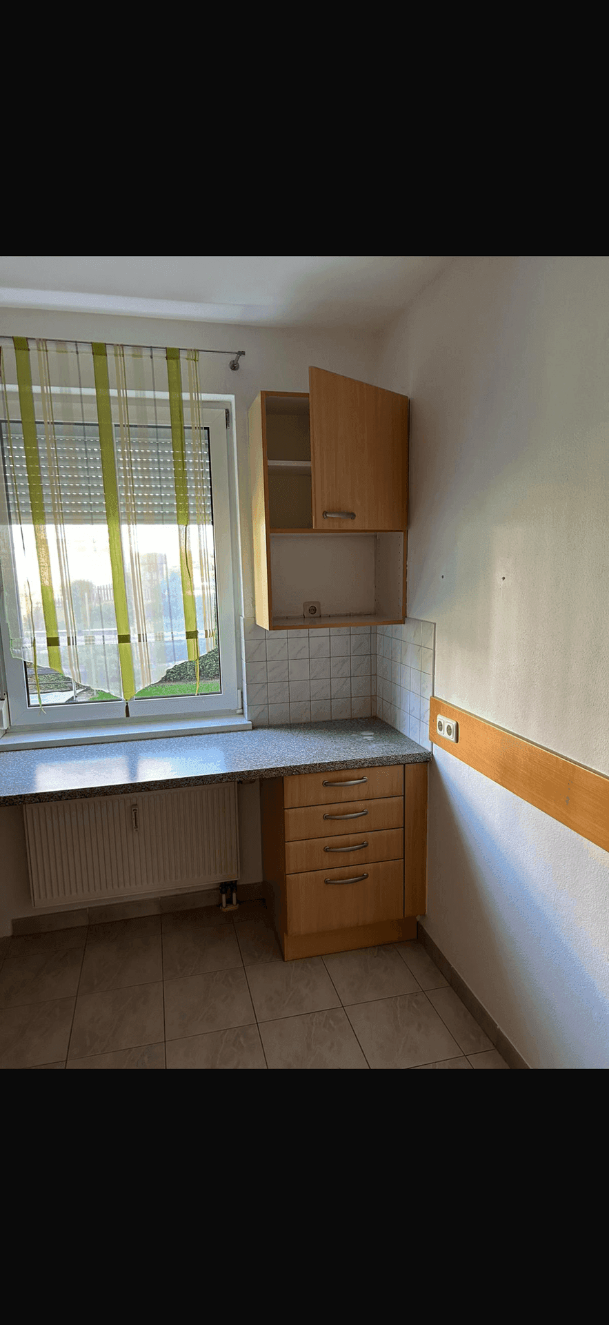 Küchenecke mit Holzunterschränken, Granit-Arbeitsplatte und Fenster mit Vorhängen.
