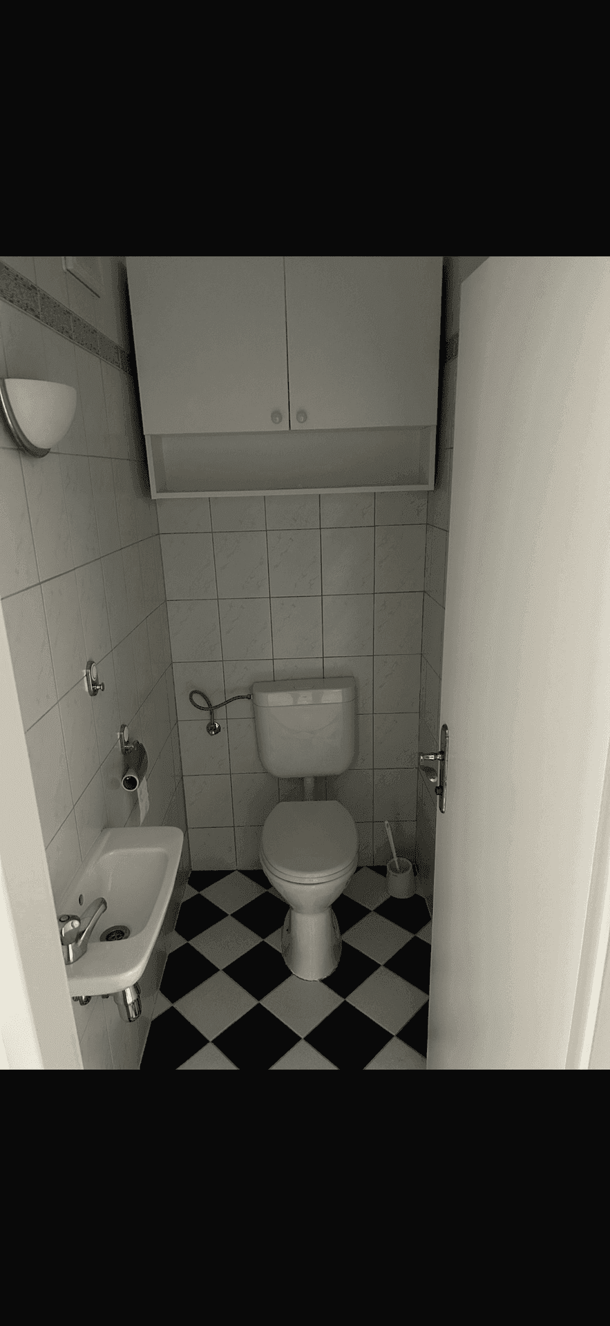 Gäste-WC mit Toilette, kleinem Waschbecken und markantem schwarz-weiß kariertem Fliesenboden.