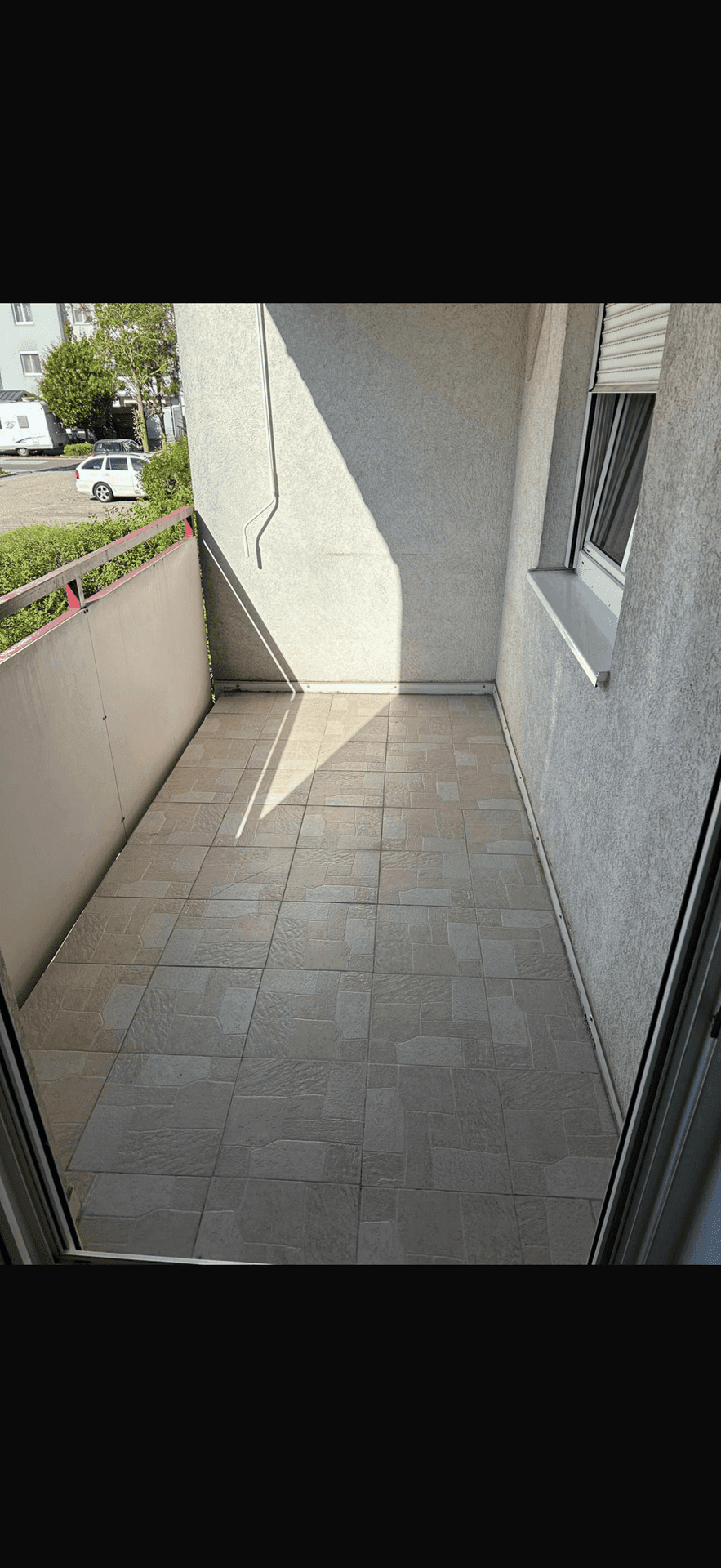 Sonniger Balkon mit Fliesenboden und Blick auf die umliegenden Gebäude und die Straße.
