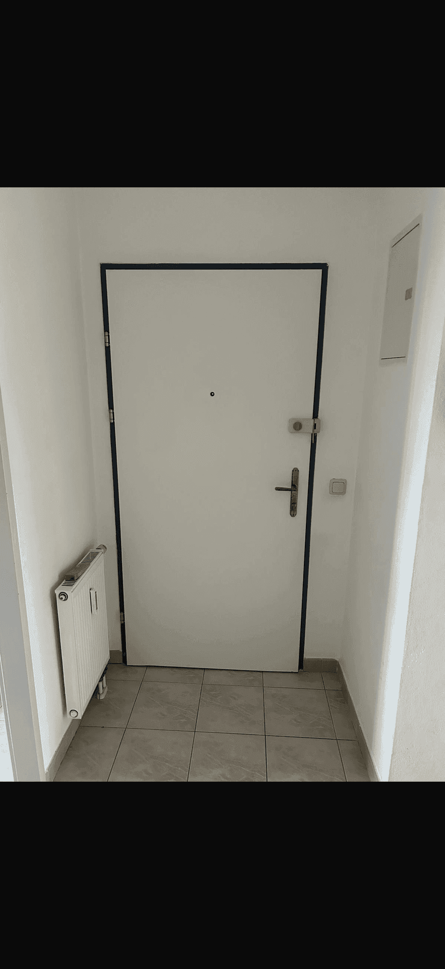 Eingangsbereich mit weißer Tür, Fliesenboden und Heizkörper an der Wand.
