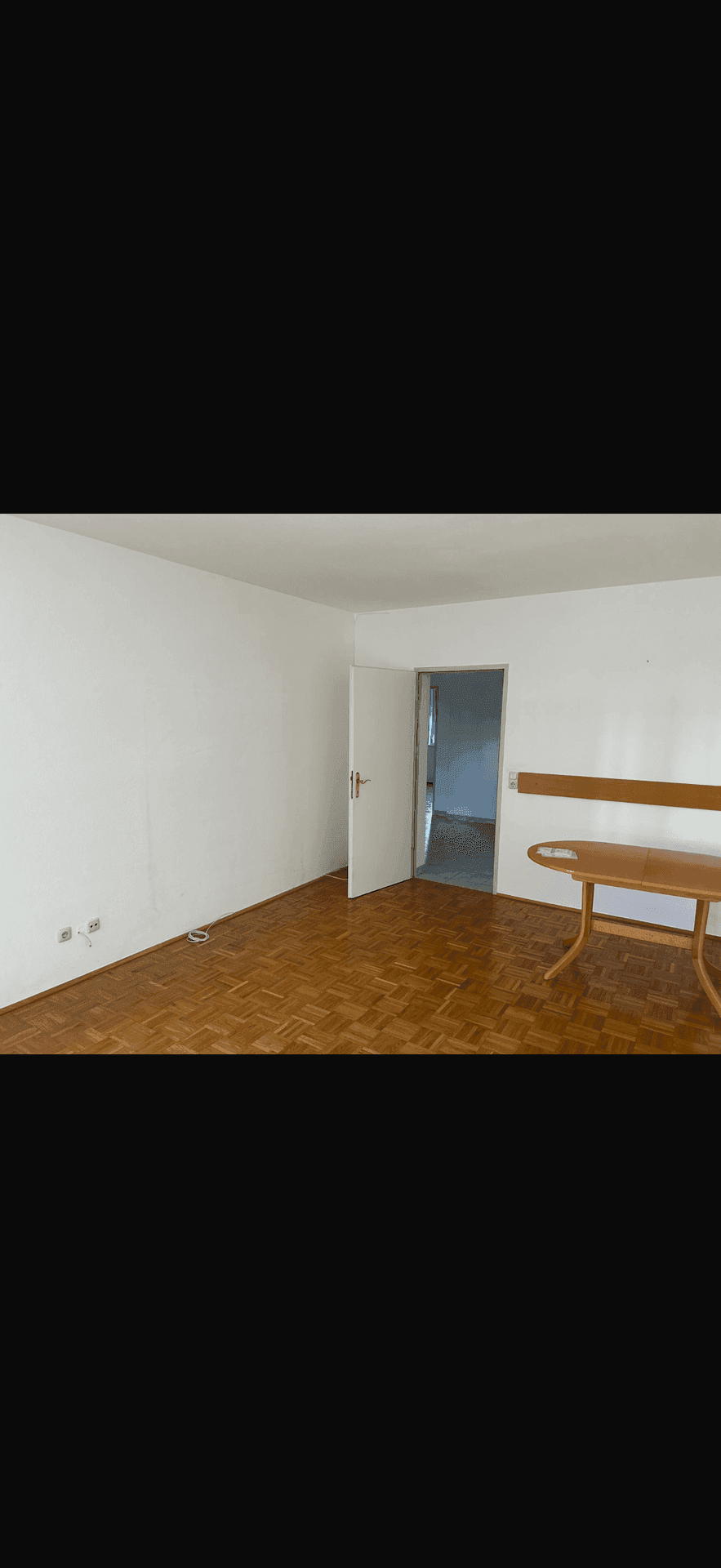 Leerer Raum mit Parkettboden und Tür zu einem weiteren Zimmer, ideal als Schlaf- oder Wohnzimmer.