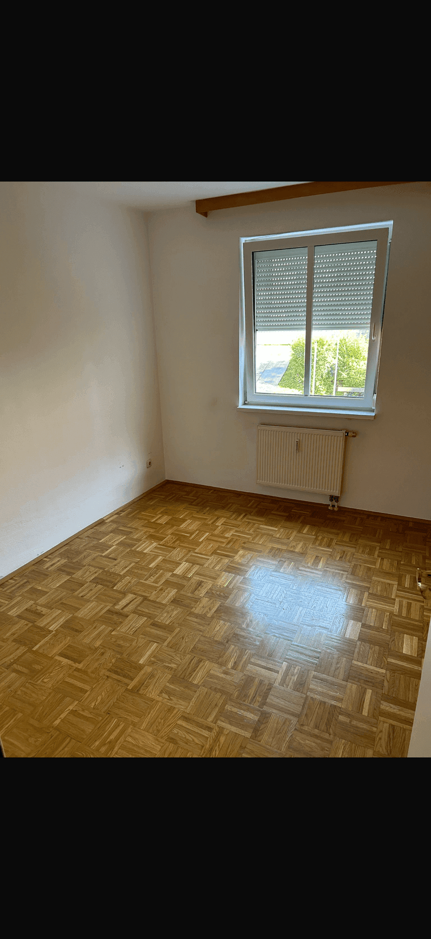 Helles Schlafzimmer mit Parkettboden, Fenster mit Rollläden und Heizkörper.