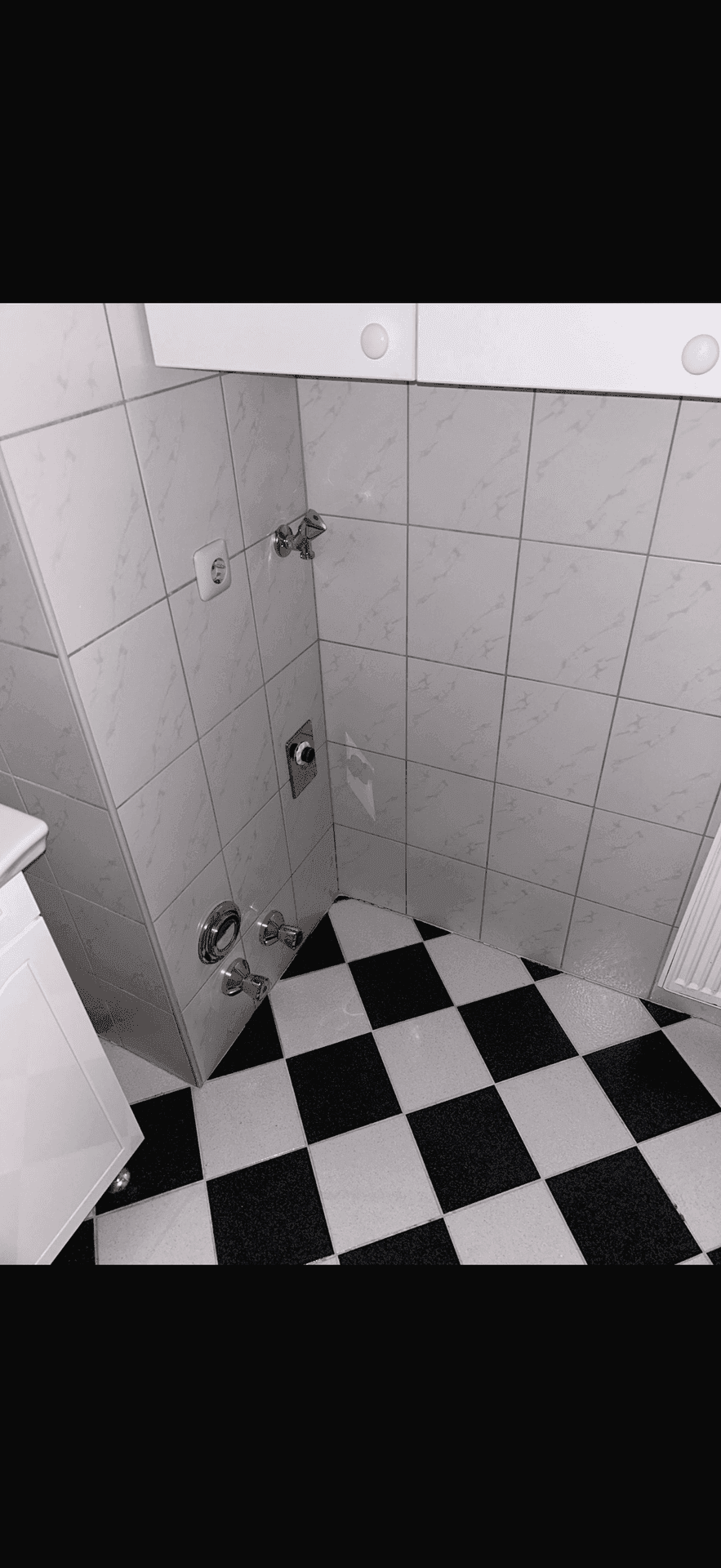 Badezimmerecke mit gefliesten Wänden, kariertem Boden und Anschlüssen für eine Dusche.