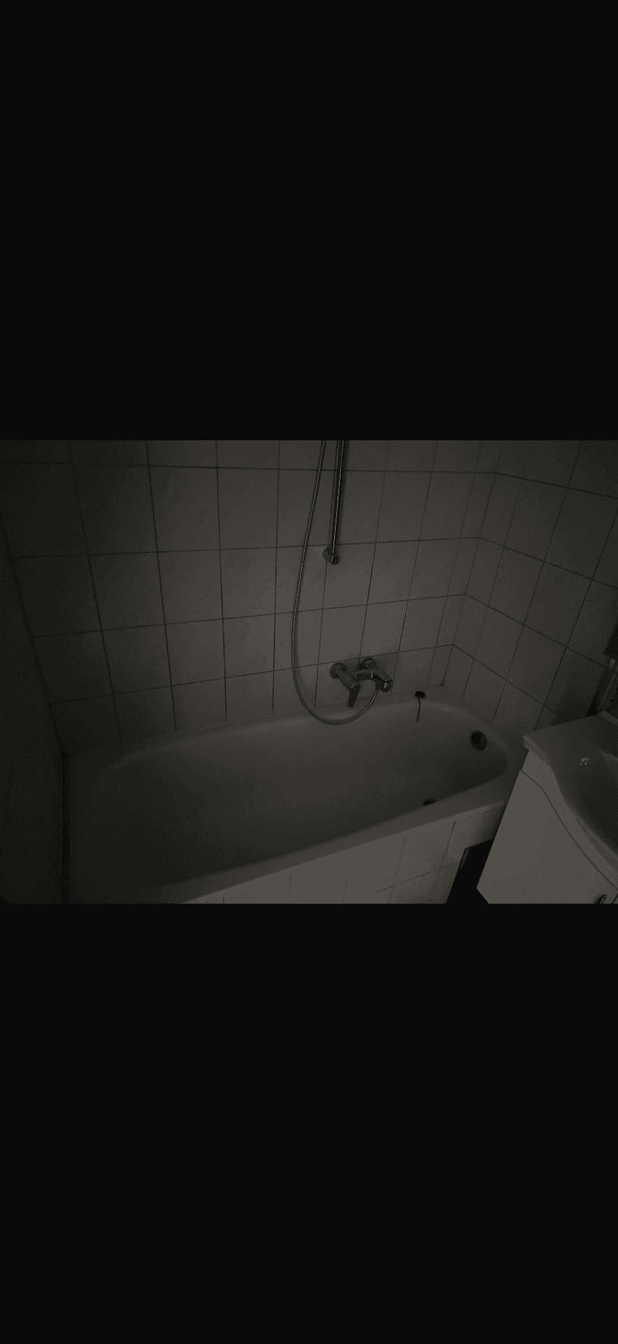 Badezimmer mit Badewanne und gefliesten Wänden, in gedämpftem Licht.