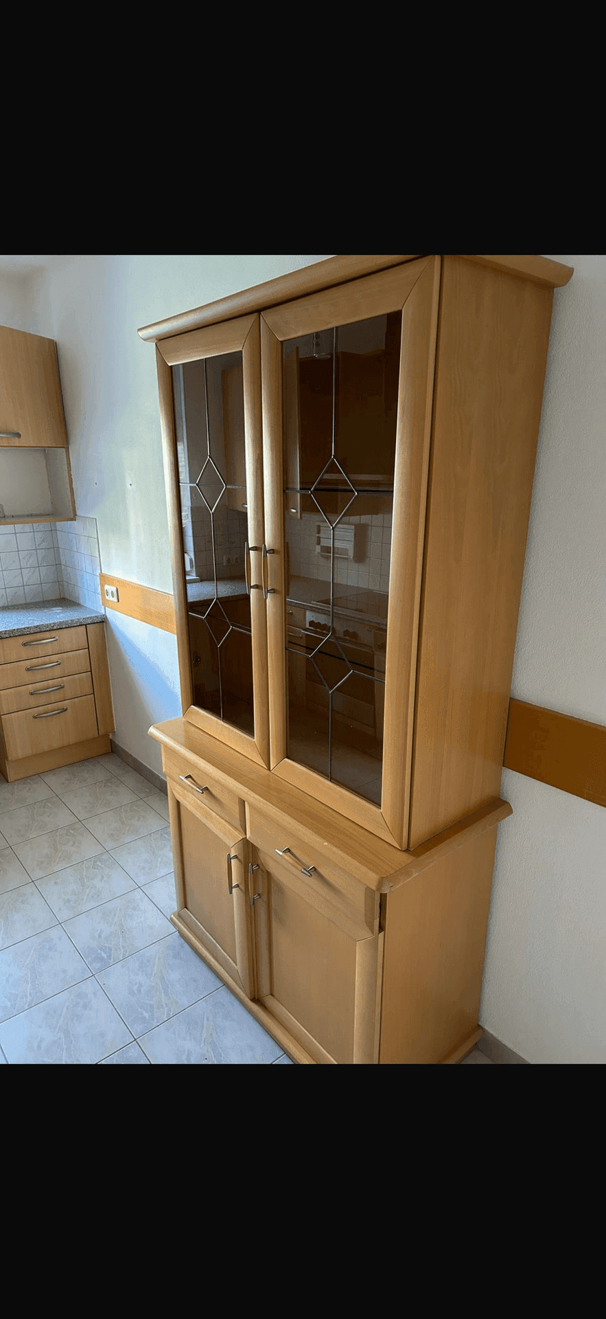 Küchenbereich mit einem klassischen Holzvitrinenschrank und Fliesenboden.